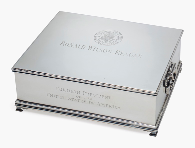 An American silver musical humidor, mark of Tiffany & Co., New York, circa 1981. The hinged top engraved with the Presidential Seal of The United States, ‘RONALD WILSON REAGAN, FORTIETH PRESIDENT OF THE UNITED STATES OF AMERICA, WITH PRIDE AND BEST WISHES ALWAYS, BOB GRAY’. Mahogany-lined, playing ‘All Hail the Chief’, marked to the underside. 3 ½ in (8.3 cm)