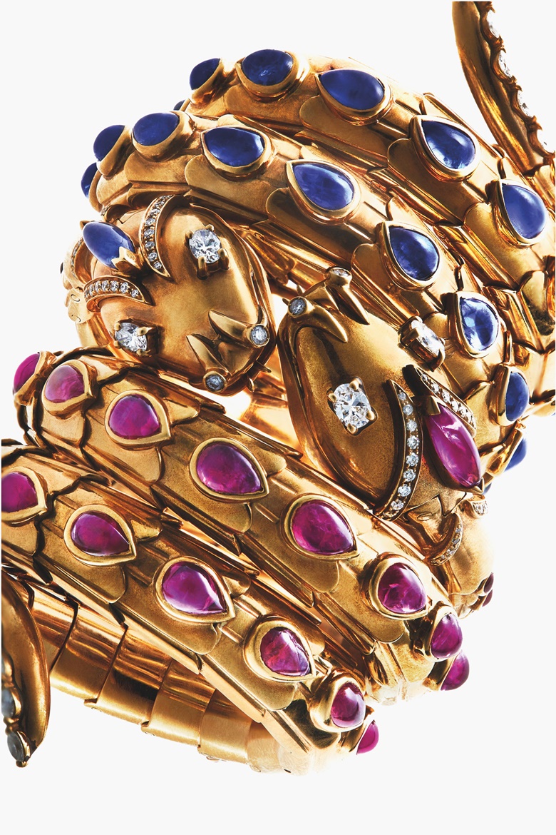 A pair of rare ruby, sapphire and diamond ‘Serpenti’ watch-bracelets, by Bulgari. Each designed as a coiled snake, the sprung body and the crest applied with cabochon ruby or sapphire, the head and tail enhanced by lines of diamonds, with oval-cut diamond eyes, the hinged jaw opening to reveal a circular dial with Arabic quarters and dagger hour markers, mechanical movement, mounted