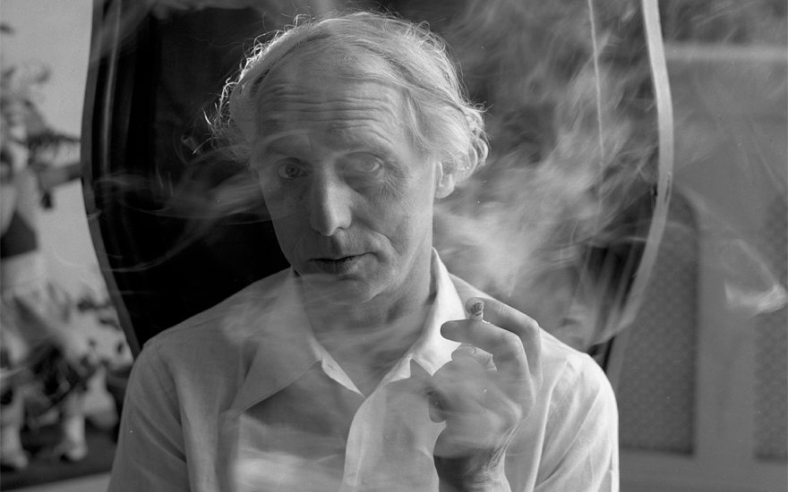 Max Ernst sits in a high-backed chair, a cigarette in his hand, in the house he shared with then-wife Peggy Guggenheim, New York, 1942, photograph by Arnold Newman