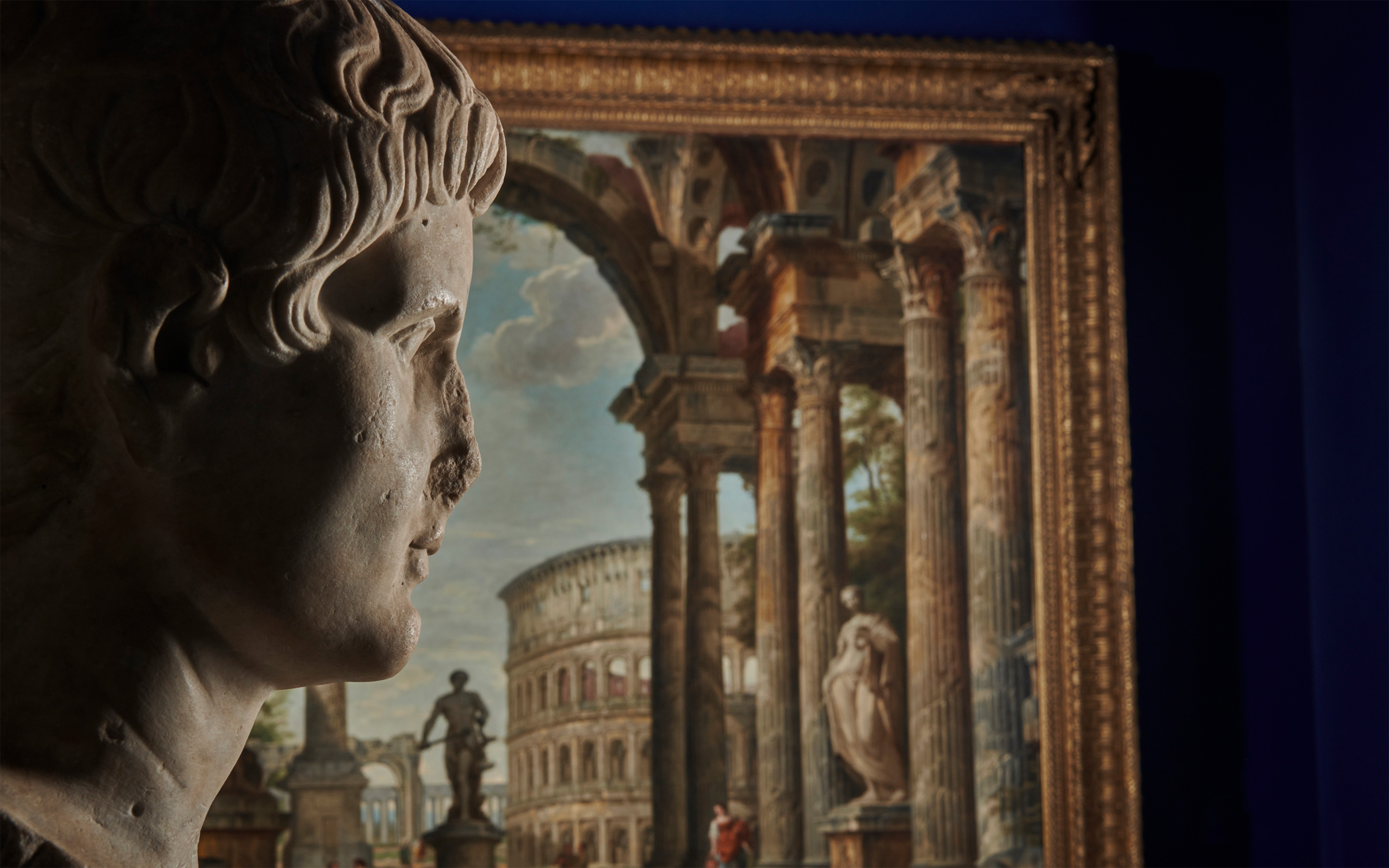 A Roman marble portrait head of the Emperor Augustus, circa early 1st century A.D. and a detail of A classical capriccio with the Colosseum, Trajan's column and the Farnese Hercules, by Giovanni Paolo Panini. Both offered in Ancient to Modern Art from the Mougins Museum of Classical Art, Part I on 7 December 2023 at Christie's in London