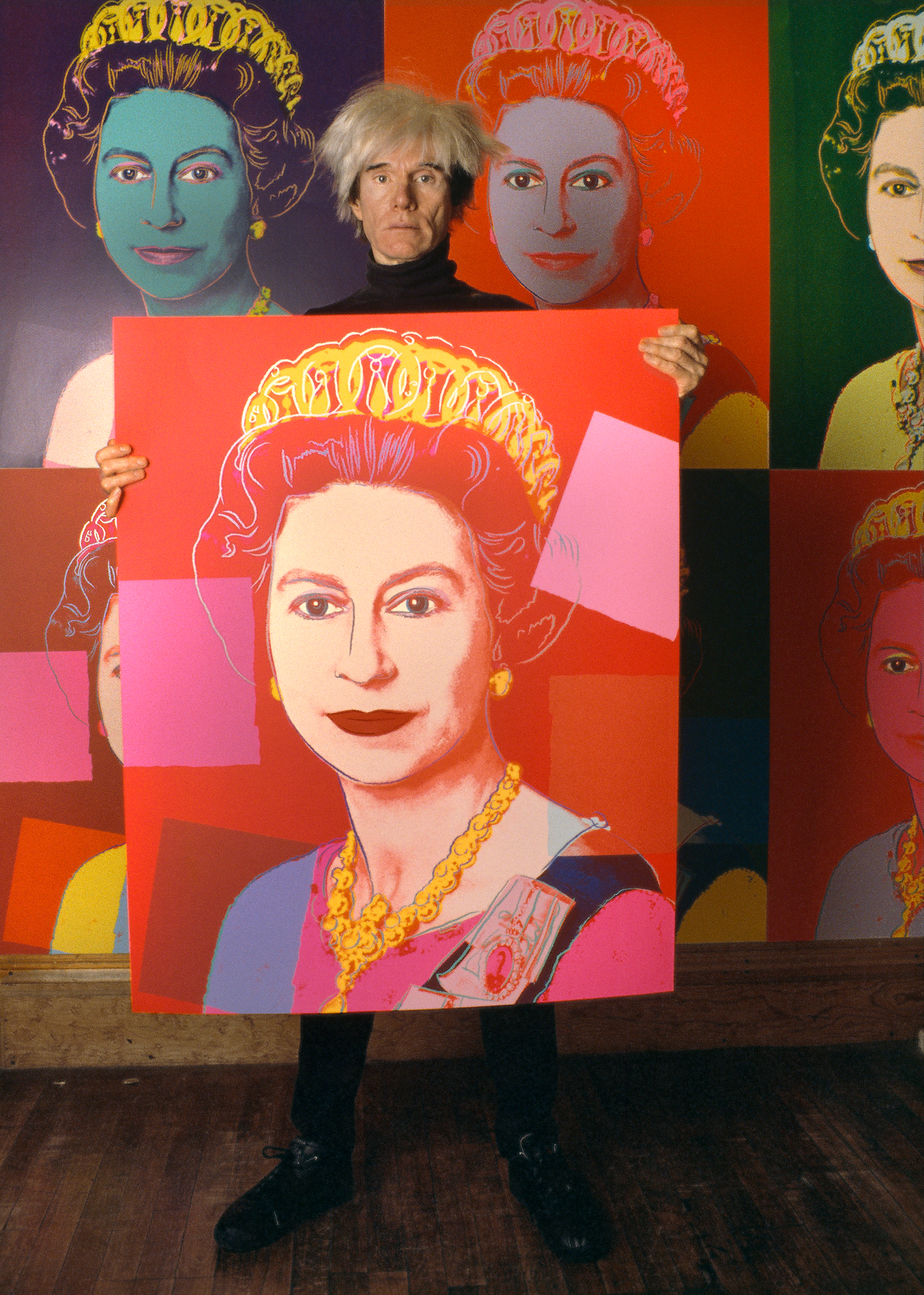 Andy Warhol holds a screenprint of Queen Elizabeth II in his studio at the Factory, New York, in 1985. The picture is part of his Reigning Queens series, others of which are on the wall behind him. Photo: Derek Hudson/Getty Images. Artwork: © 2022 The Andy Warhol Foundation for the Visual Arts, Inc / Licensed by DACS London
