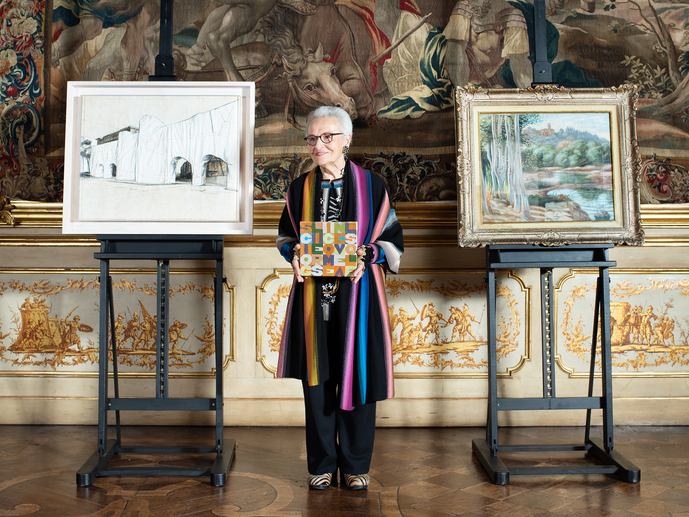Rosita Missoni holding Alighiero Boetti’s Sciogliersi come neve al sole (Melting Like Snow in the Sun), 1989, and flanked by Christo, The Wall (Project for a Wrapped Roman Wall — ‘Porta Pinciana’ delle Mura Aureliane, Via Vittorio Veneto and Villa Borghese), 1974 (left), and Giorgio de Chirico, Paese (La certosa), 1931-32 (right). Photo: Martina Giammaria