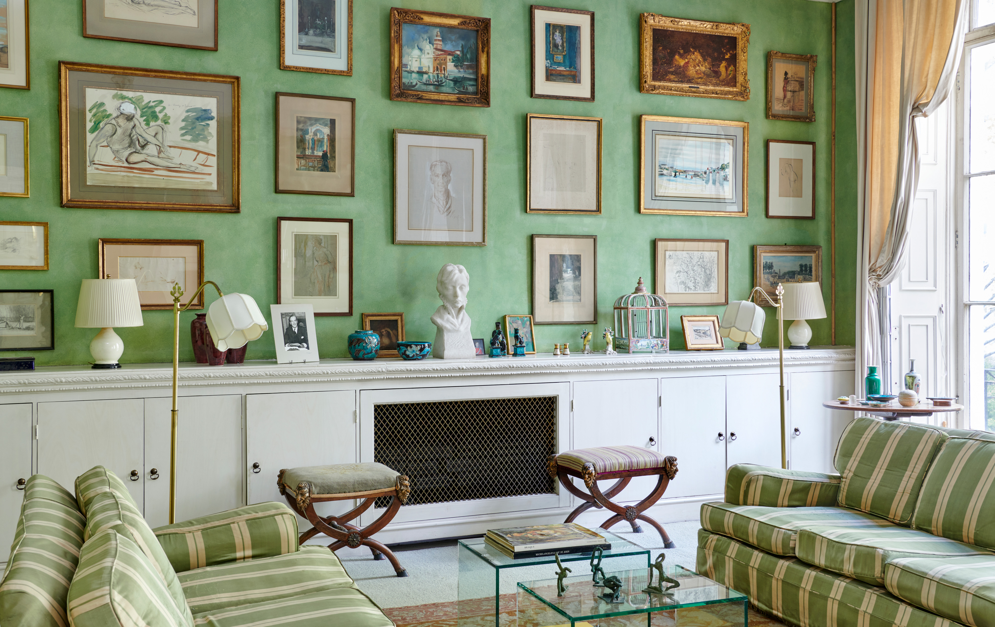 Works of art, objects and furniture in the drawing room, including a pair of north Italian mahogany and parcel-gilt X-frame stools, and a group of Chinese Fahua porcelain vessels and figures. On the coffee table is a group of four figures by Ivor Abrahams, R.A. Offered in Churchill to Eden: The Collection of The Earl and Countess of Avon on 21 October 2022 at Christie’s in London