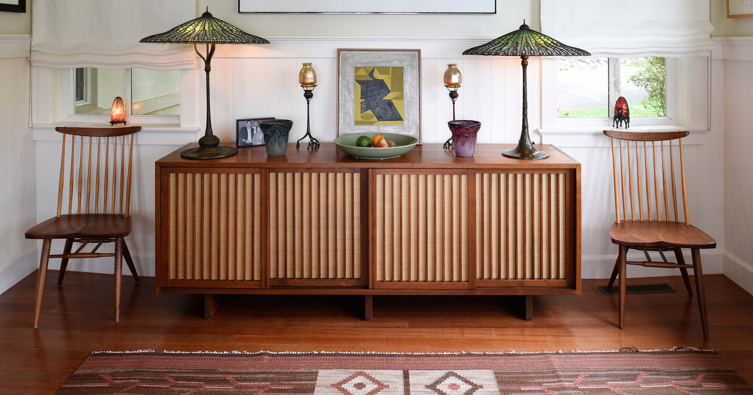 Atop a Nakashima cabinet are lamps and candlesticks by Tiffany Studios and a Victor Vasarely painting