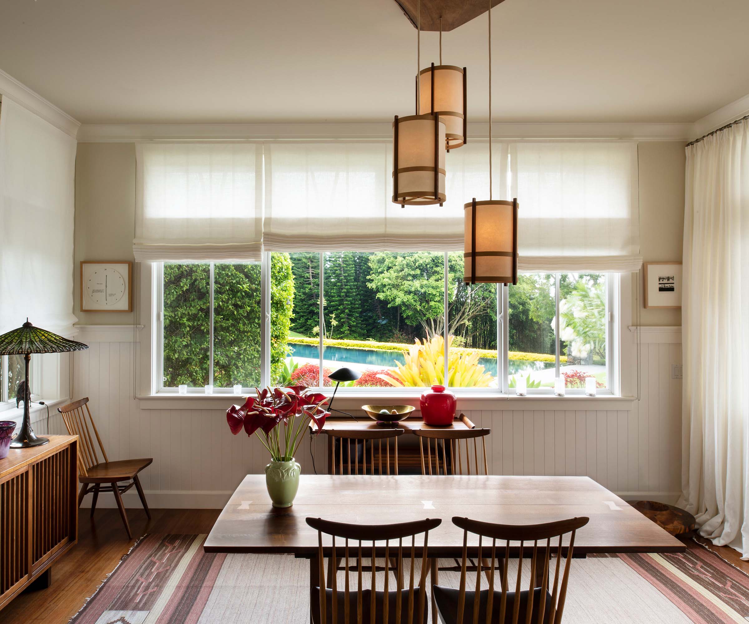 A custom George Nakashima chandelier hangs above a Nakashima table and chairs in the dining room, which provides views of the verdant gardens beyond