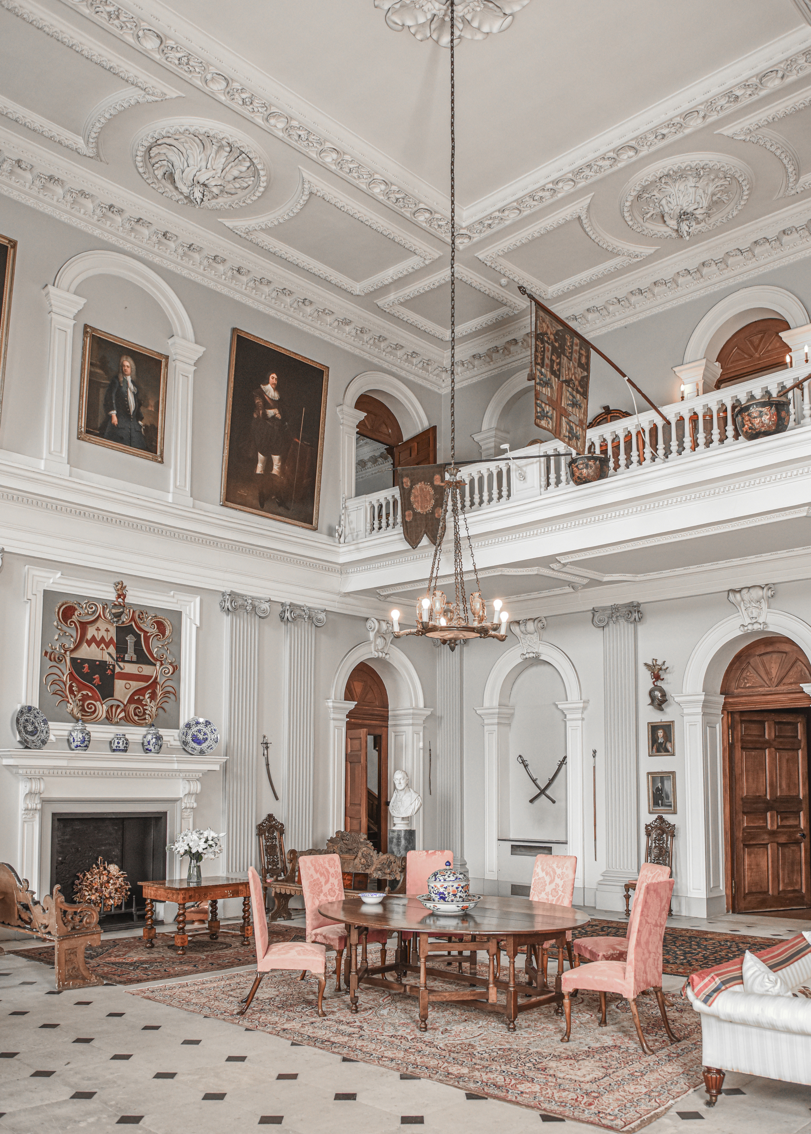The Great Hall at Ormbersley Court, including a set of George I walnut furniture, a portrait of Montague Blundell, 1st Viscount Blundell, a painted and gilt silk heraldic banner and an English or Flemish close helmet, all offered in Ombersley Court: The Collection of Lord and Lady Sandys on 29 November 2023 at Christie’s in London