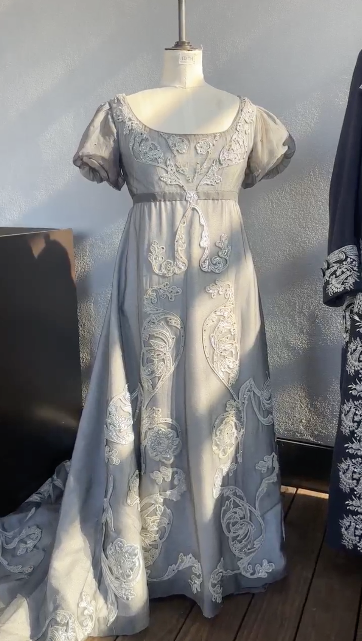 A vintage gray dress with intricate white embroidery displayed on a mannequin.