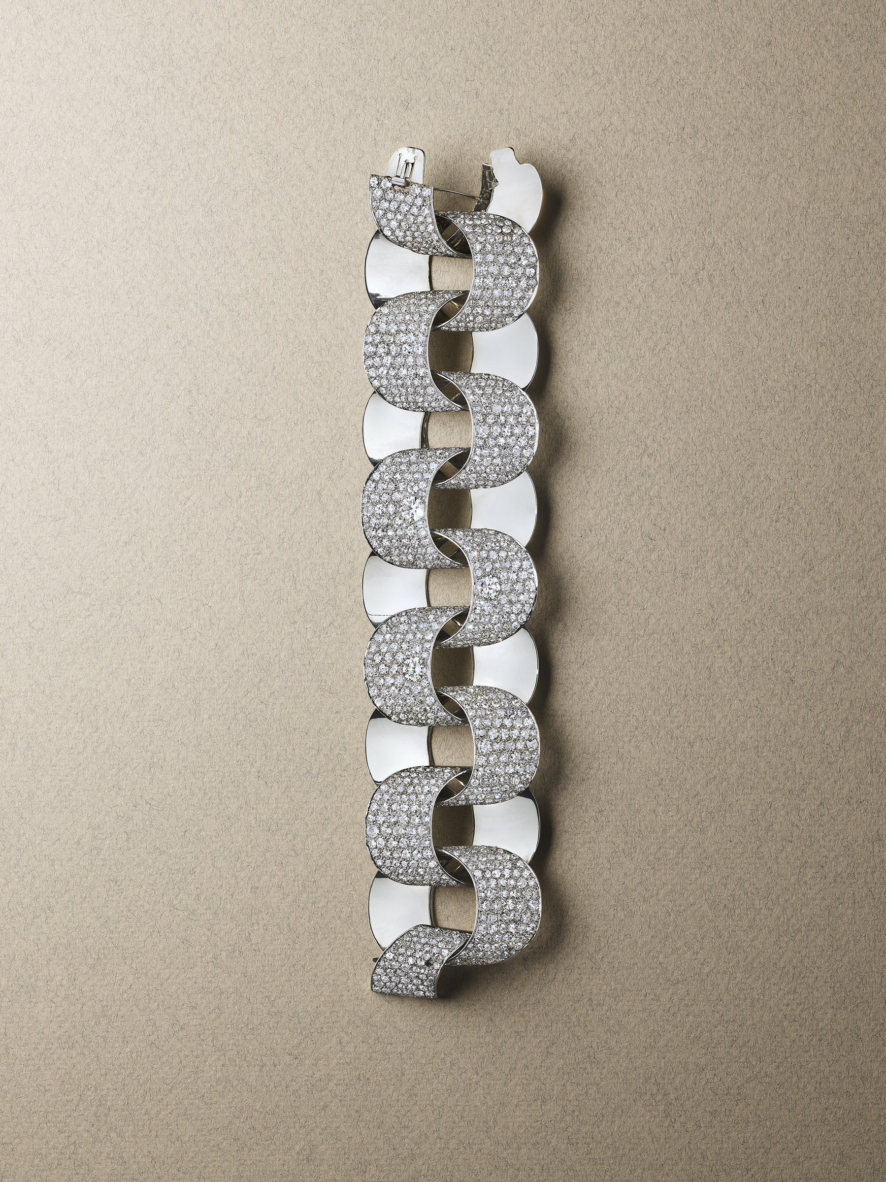 An elegant, spiraling silver bracelet adorned with numerous small diamonds, displayed on a beige background.