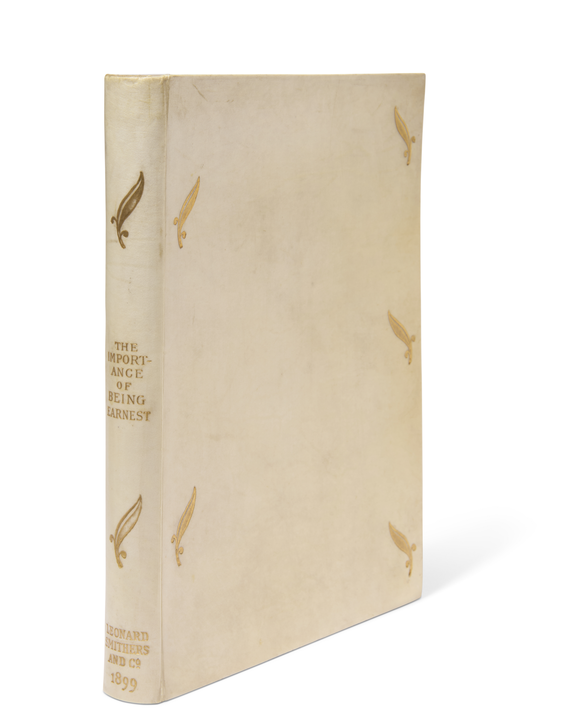 Photo of a vintage white book titled "The Importance of Being Earnest" by Leonard Smithers and Co, dated 1899, adorned with gold quill illustrations.