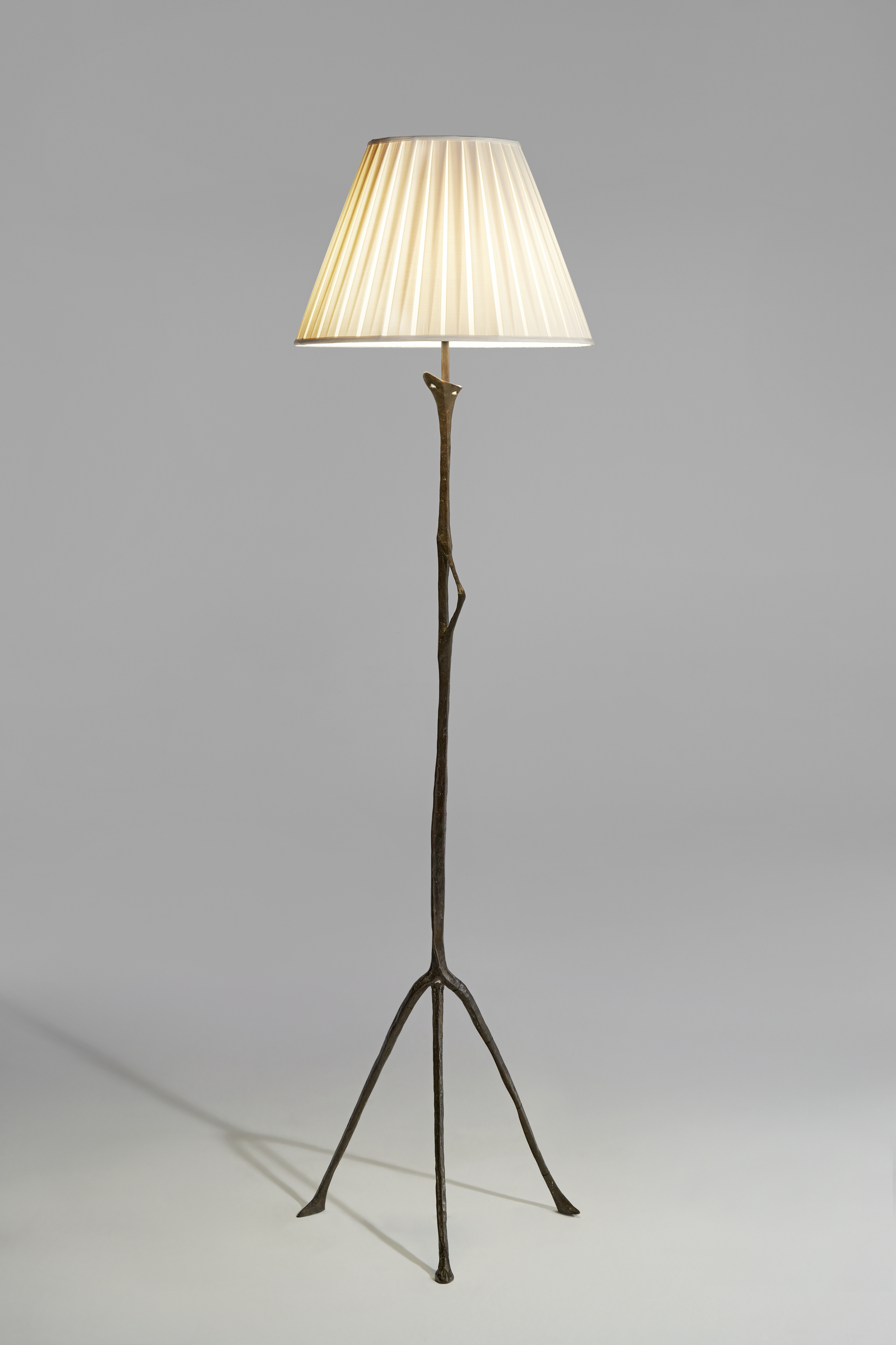 A standing lamp with a pleated lampshade and slender, branch-like metal stand.