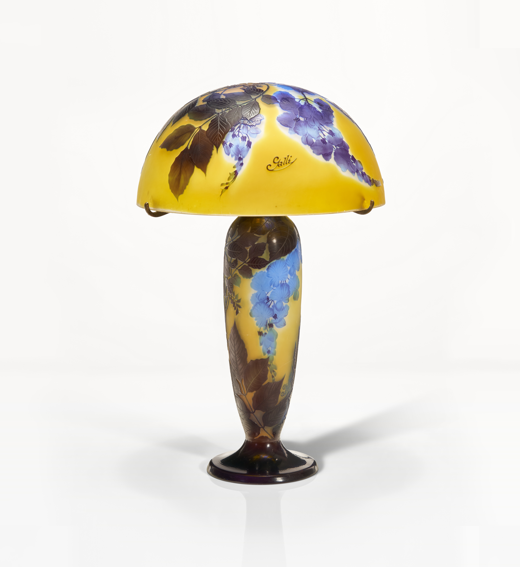 An elegant glass lamp with a dome-shaped, yellow and blue floral designed shade and a slender, leaf-patterned base.