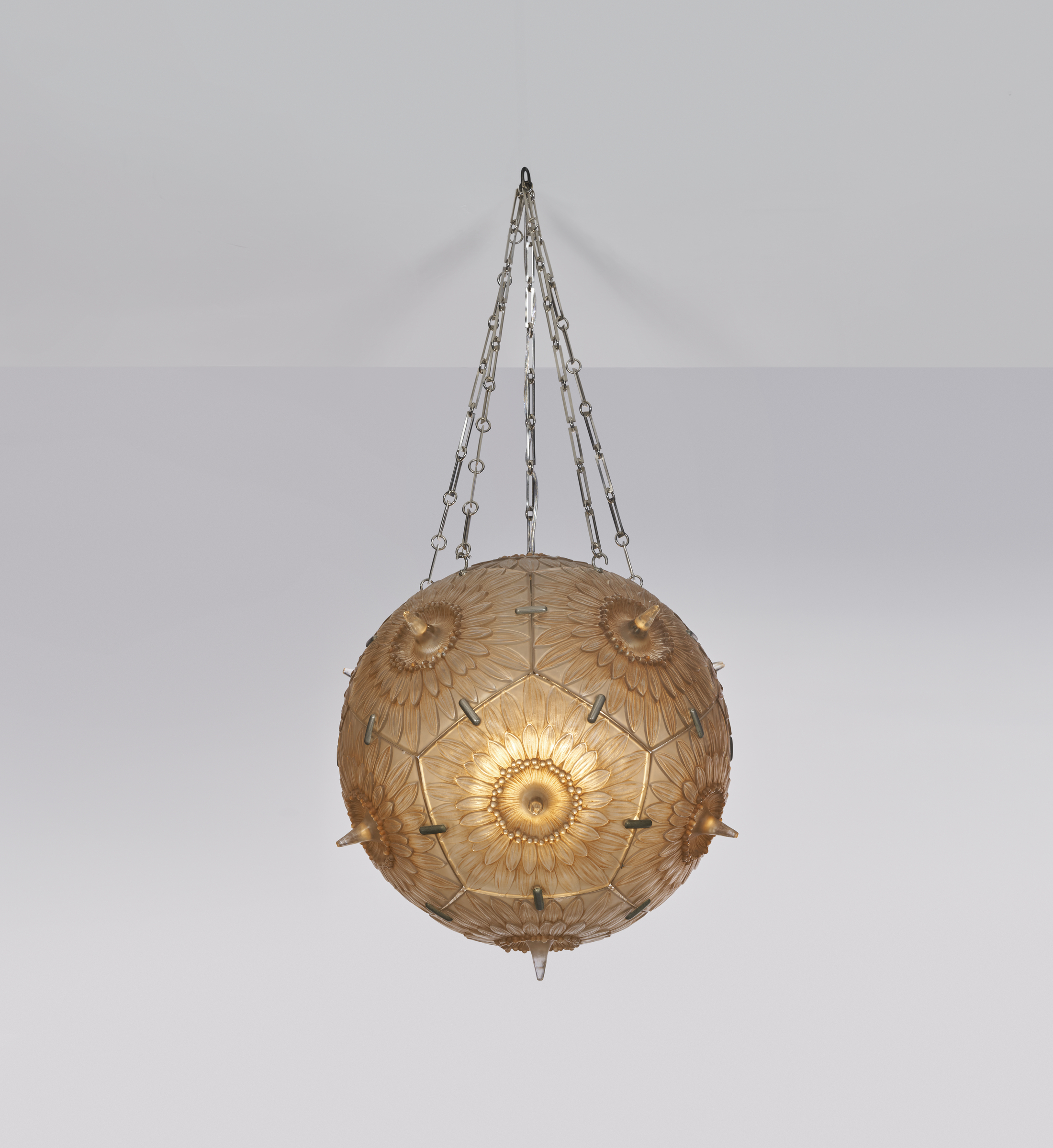 A spherical chandelier with a floral pattern hanging by chains, emitting a soft glow.
