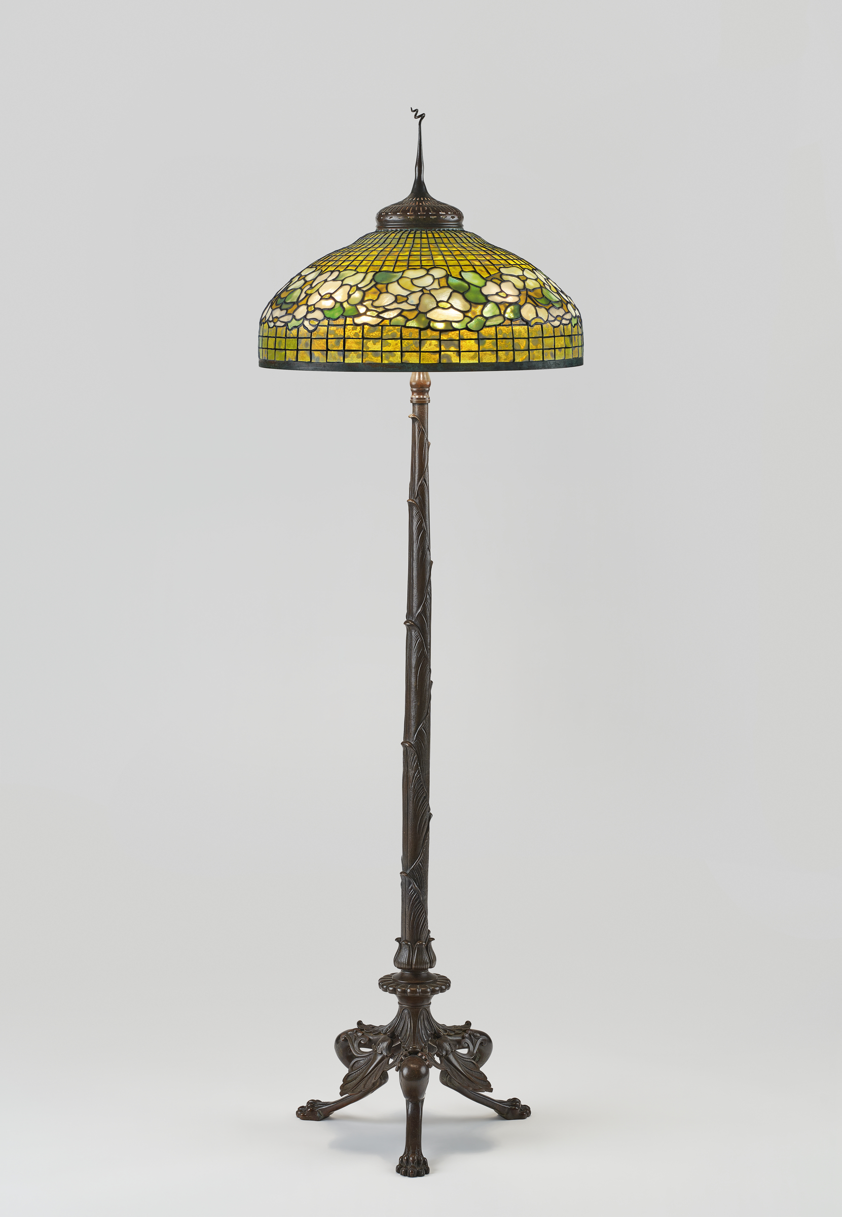 An elegant floor lamp with a stained glass shade featuring a floral design and a detailed bronze base.
