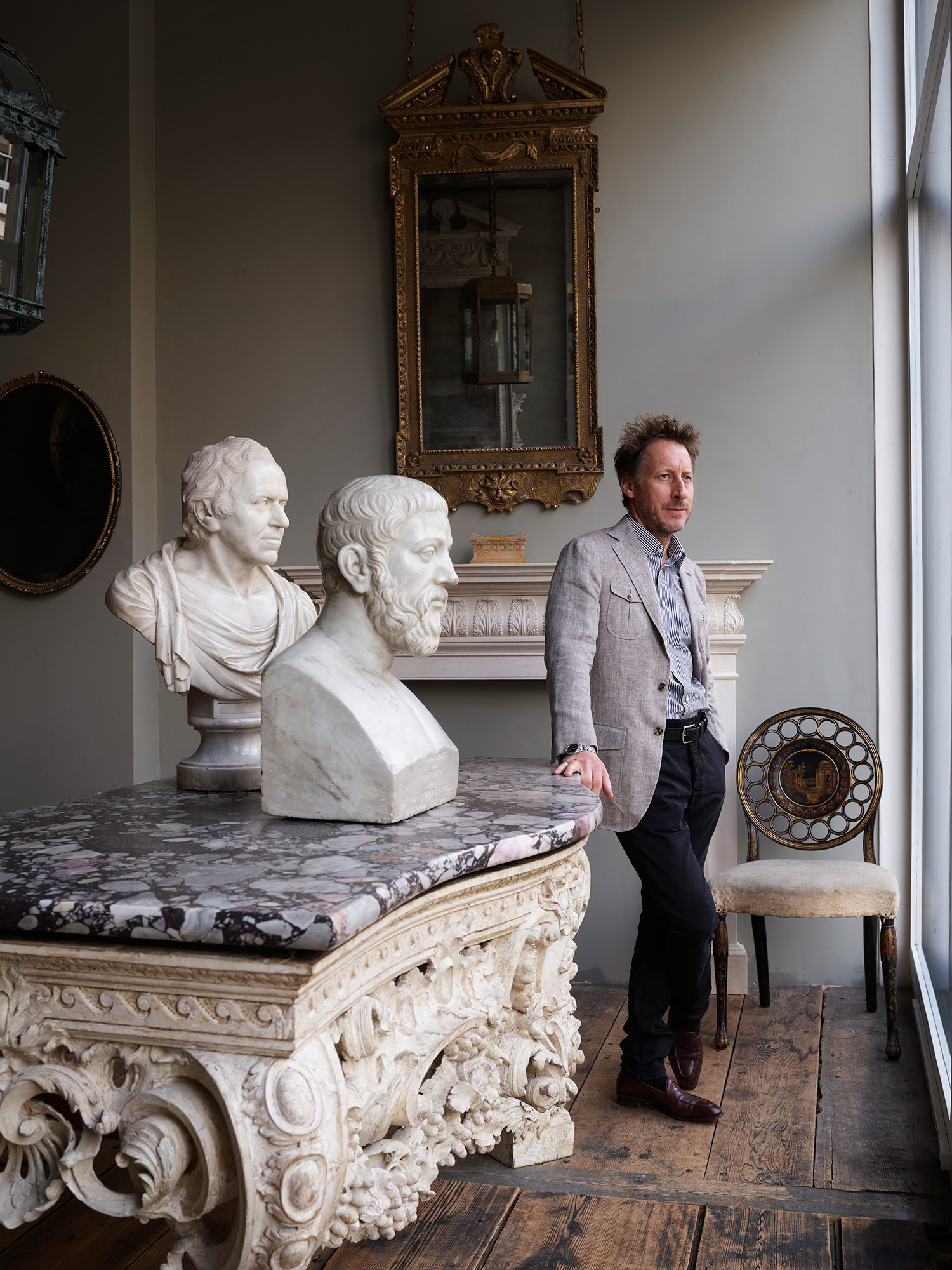 Will Fisher at Jamb's premises on Pimlico Road in London. Behind him is an Isola stone chimneypiece by Jamb, which features an acanthus-leaf frieze. The 19th-century bust of a bearded scholar on the console is available from Hawker Antiques