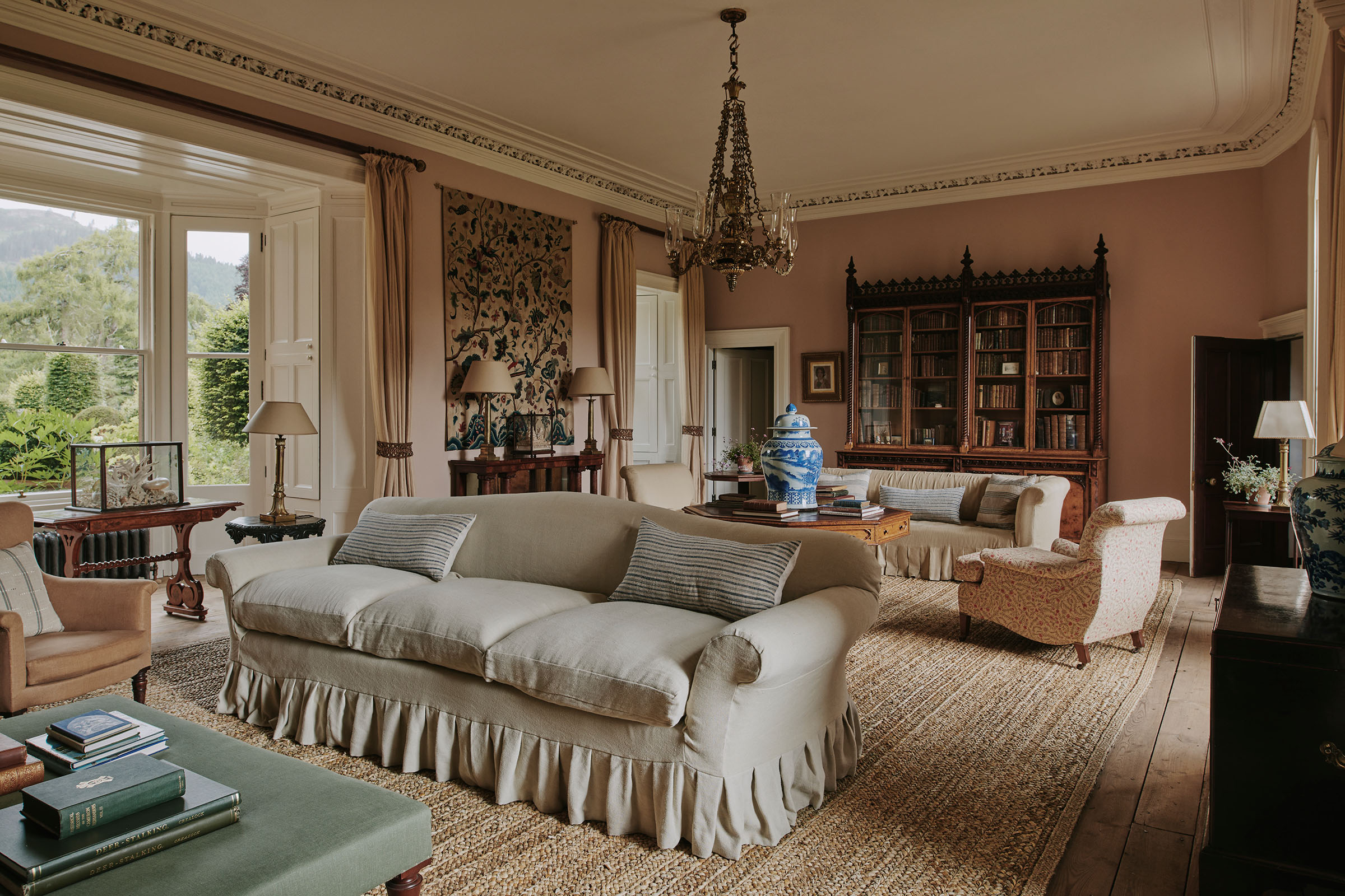 A colza-oil chandelier by Messenger and Sons hangs in the Great Hall at Aldourie Castle on the shores of Loch Ness, where pieces by Jamb include the Upton sofa in the foreground and the Crawford sofa behind, both reproductions of 19th-century originals