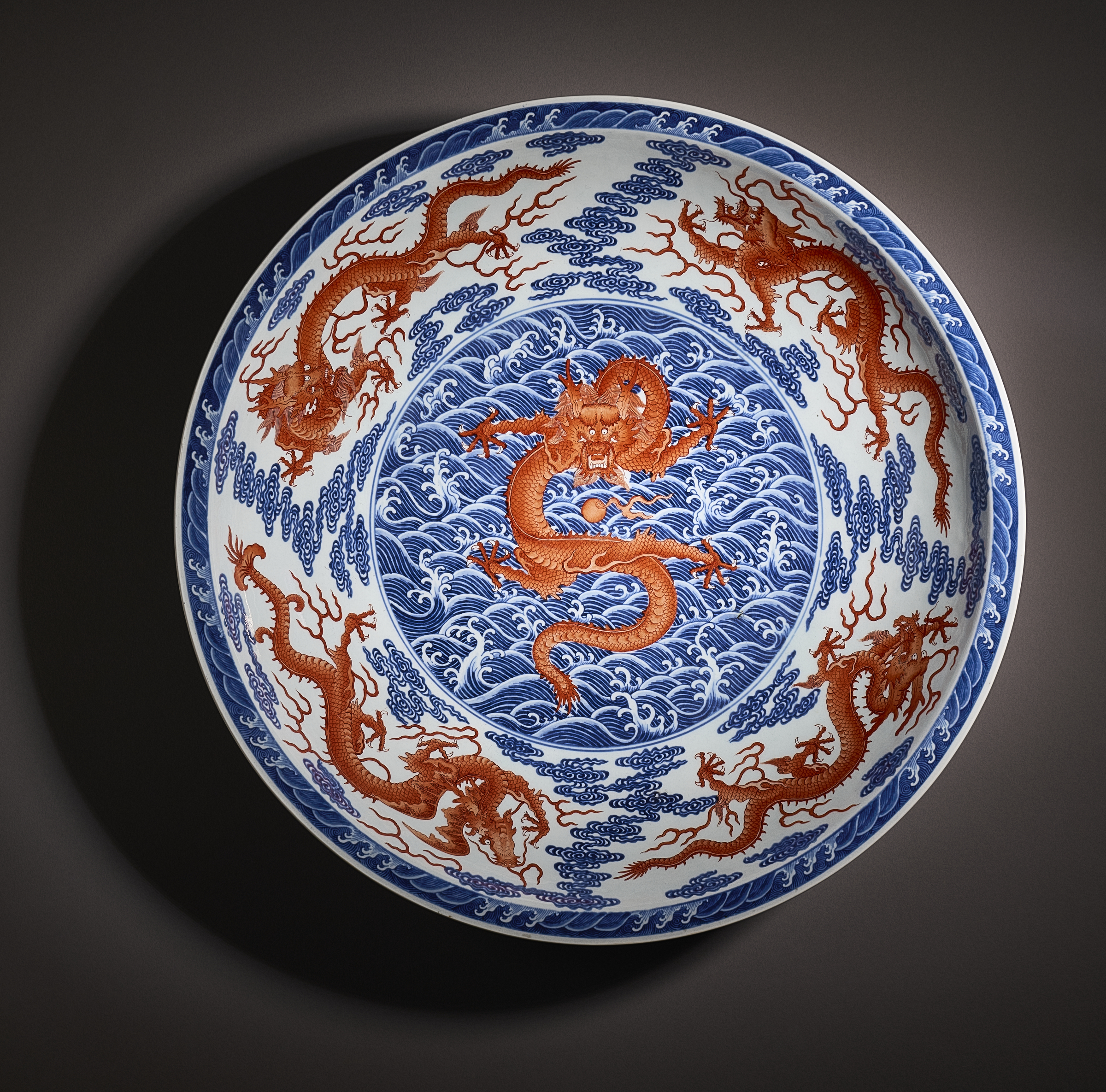 The image depicts a decorative plate featuring intricate blue and red designs of dragons amid swirling waves.