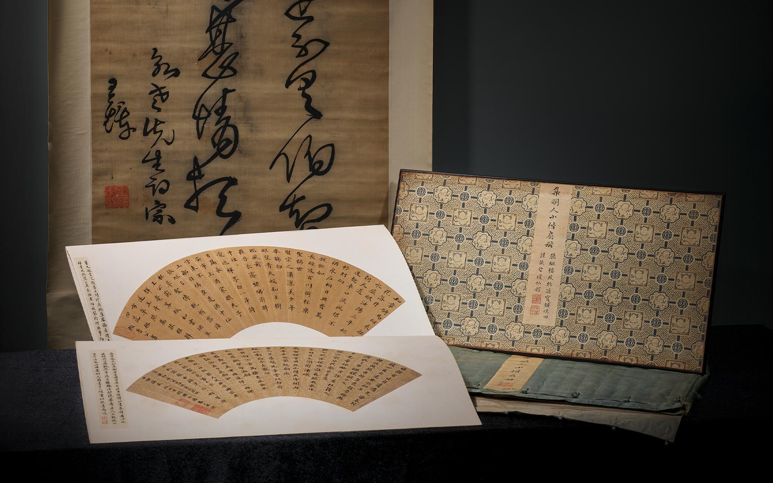 Various Asian calligraphy and printed texts displayed, including a large scroll, a book, and fan-shaped papers.