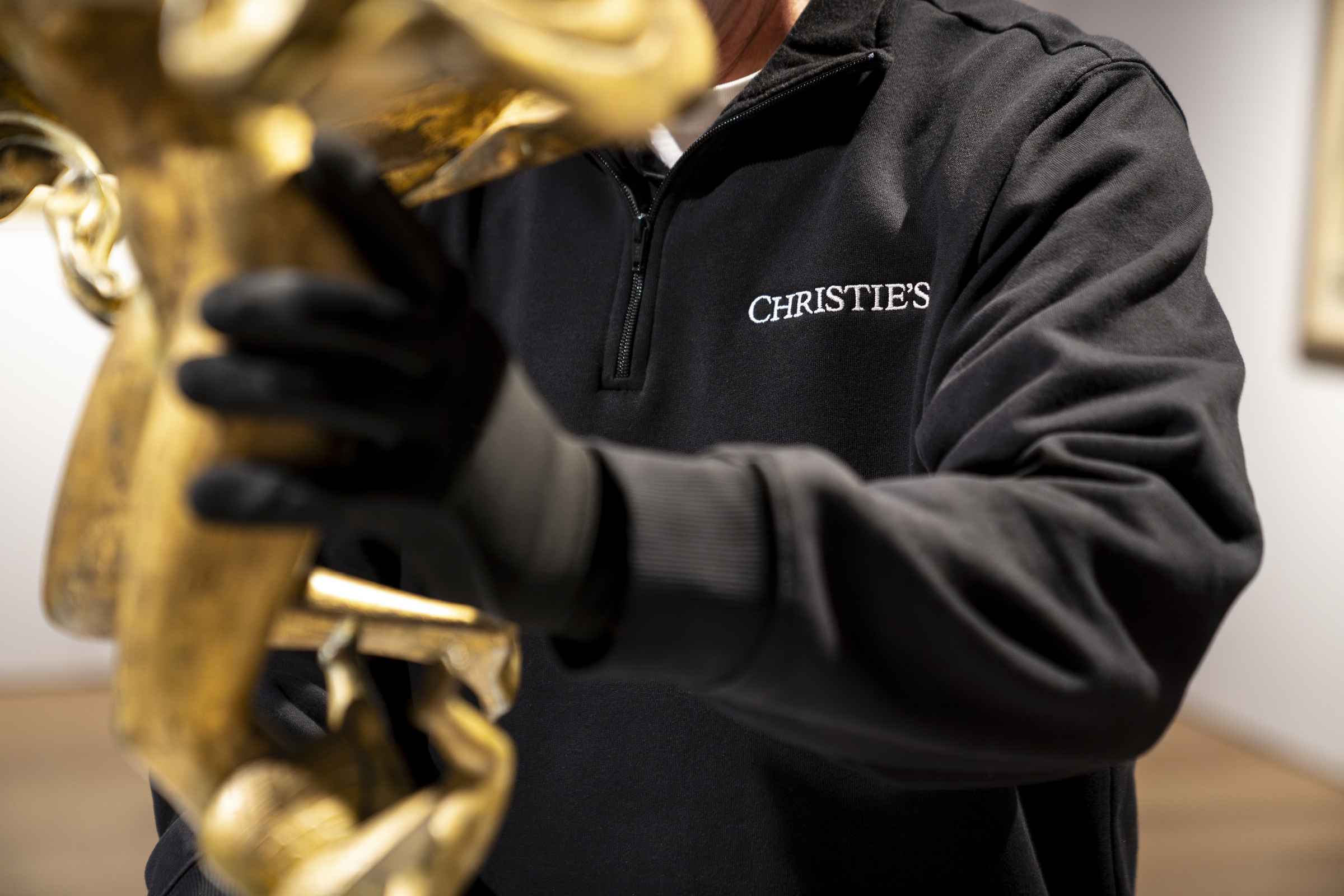 A person wearing gloves holds a golden statue, wearing a jacket with the Christie's logo.
