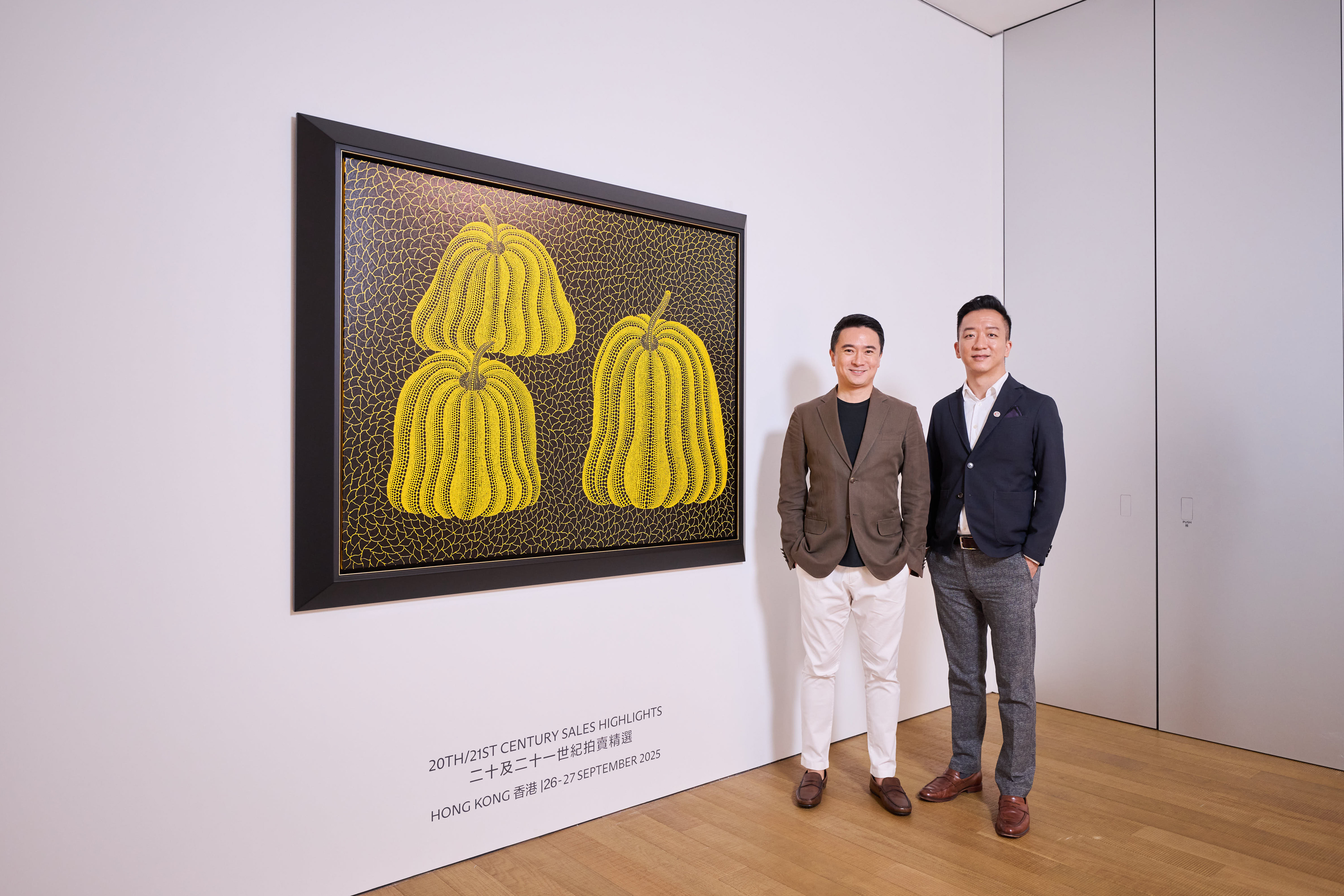 李小明与郑景康在佳士得The Henderson亚太区总部艺术空间中一同欣赏二十及二十一世纪拍卖预展。艺术作品：草间弥生，《南瓜[TWAQN]》，压克力 画布，2015年作。估价：港元22,000,000-32,000,000。此作将于2025年9月26日在佳士得香港二十及二十一世纪晚间拍卖中呈献