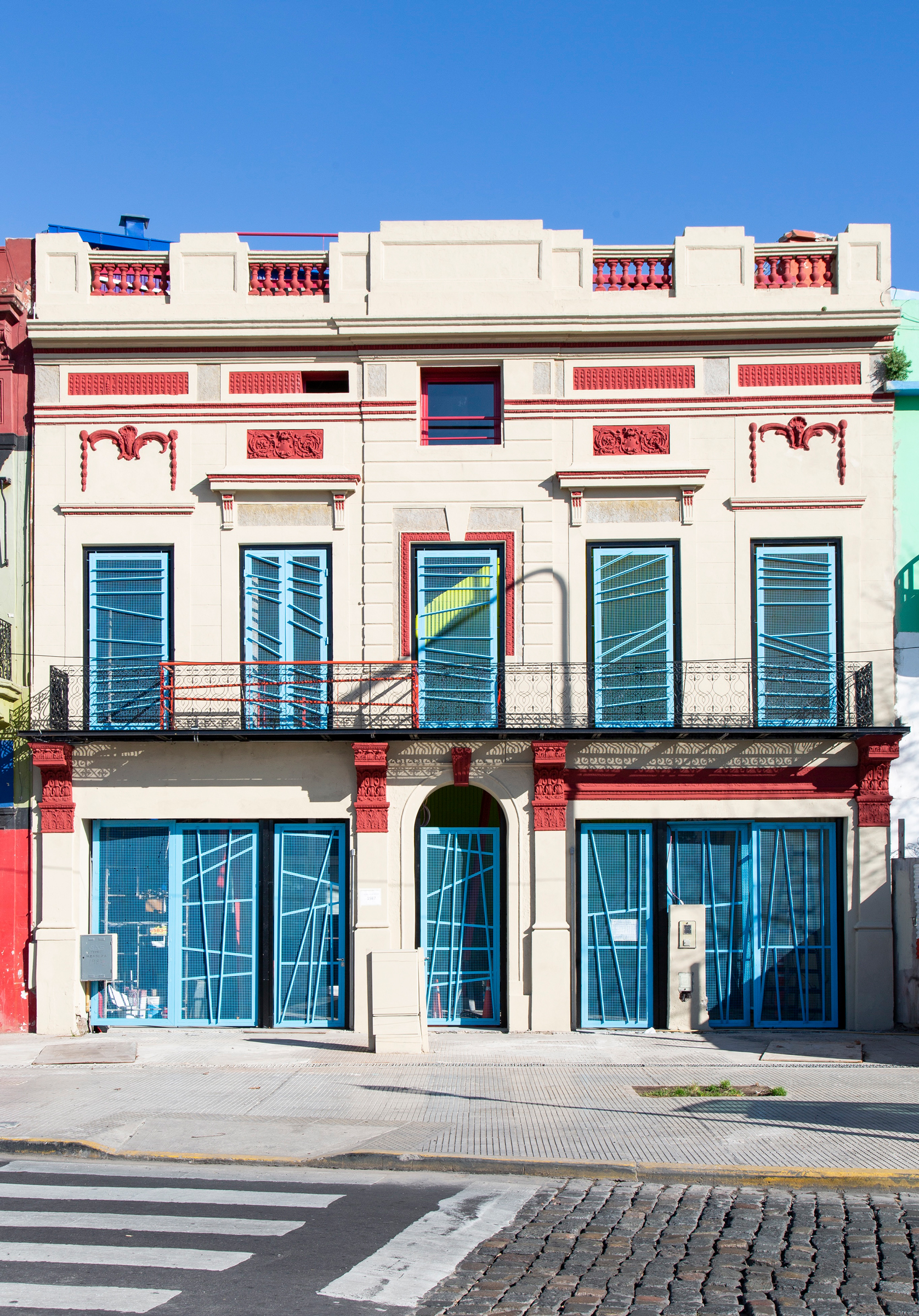 A colorful two-story building with ornate architectural details and large blue doors, positioned on a sunny street corner.