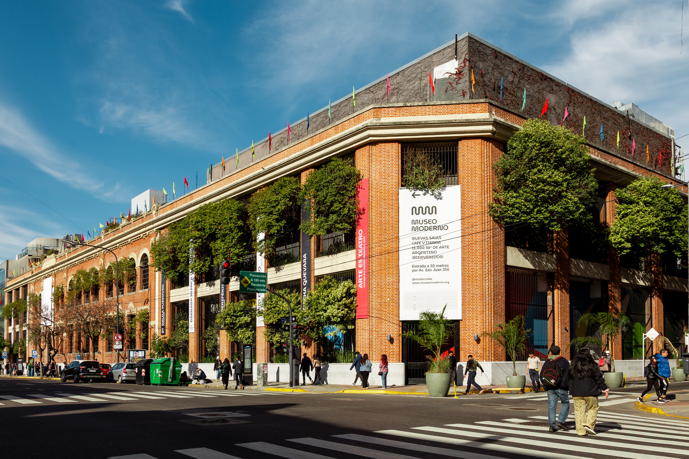A vibrant street scene in front of the brick facade of the Museo Moderno, adorned with colorful flags and banners.