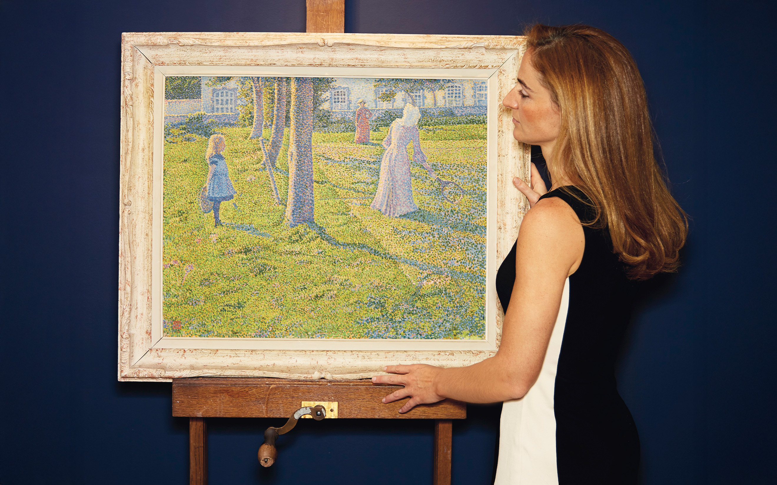 Valérie Didier views an Impressionist painting of figures in a garden with abundant blue flowers and trees.