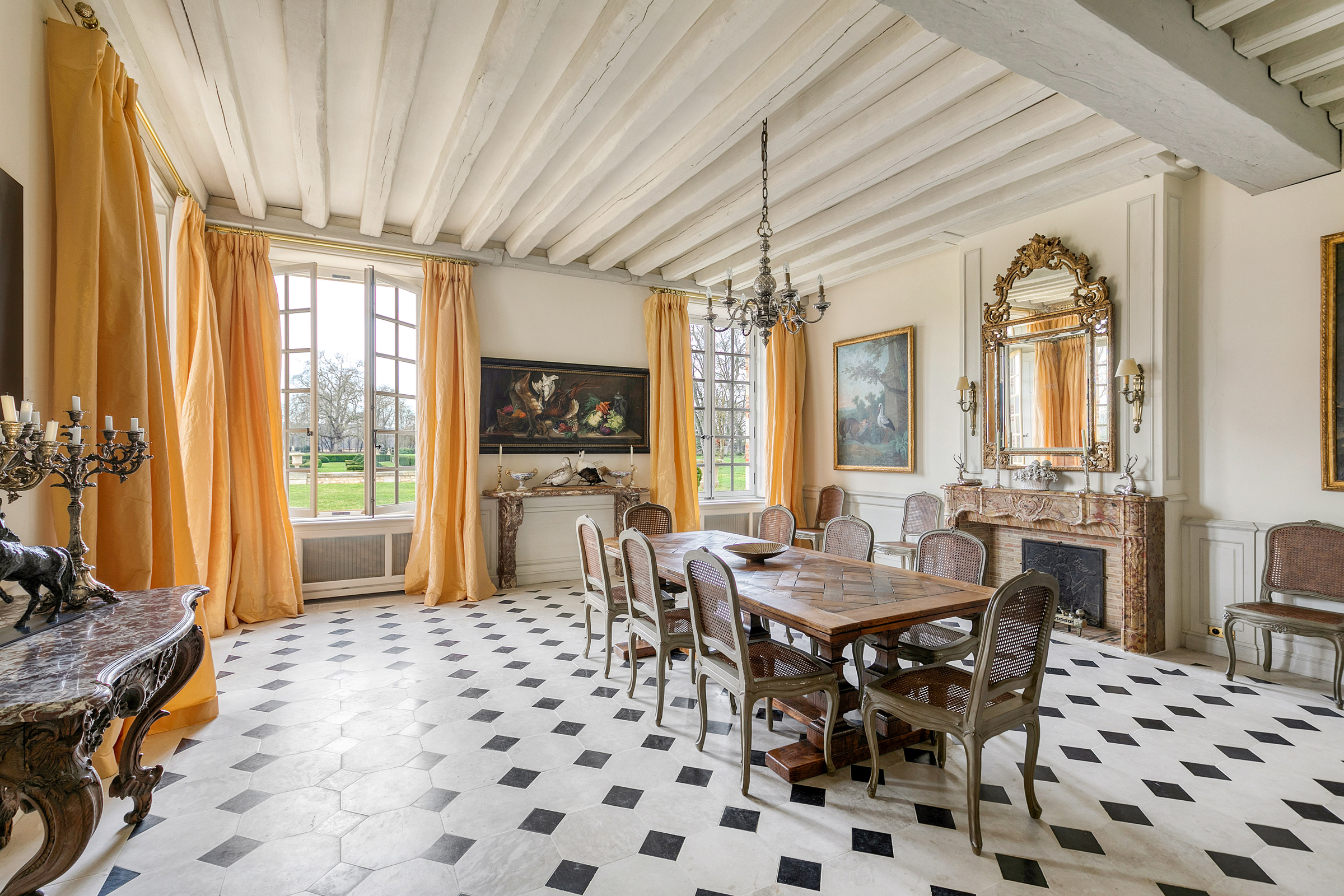 Elegant dining room with checkerboard floor, large windows with yellow drapes, and antique furnishings.