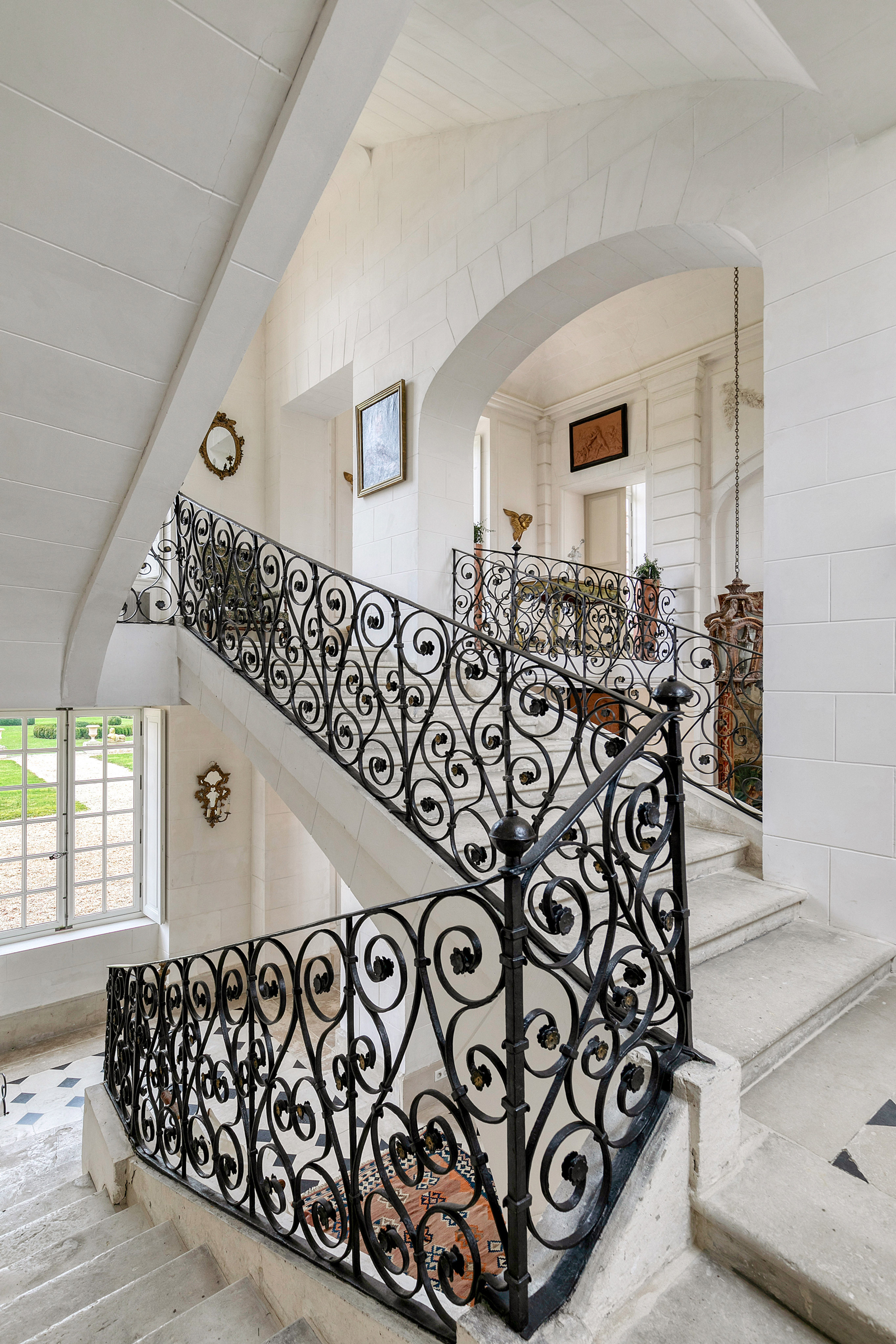 Elegant interior staircase with ornate black railing and arched white walls, enhanced by framed pictures and decorative elements.