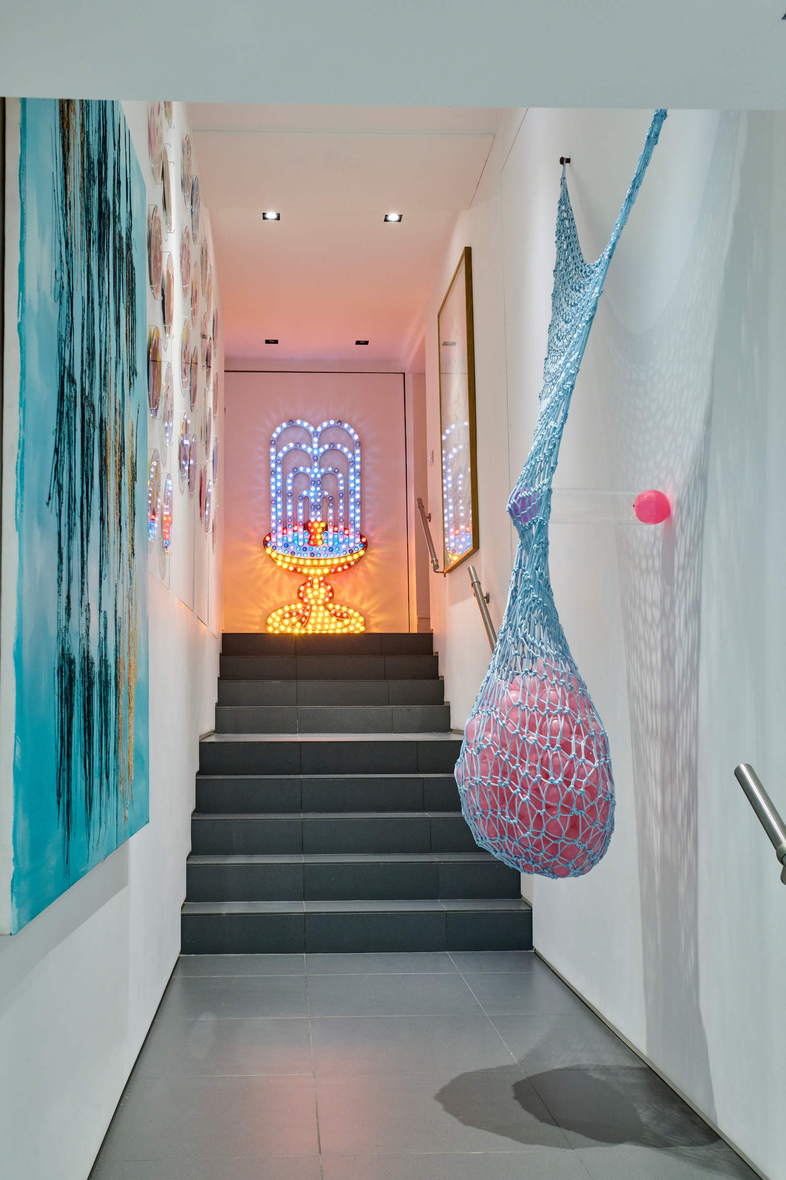 Crowning the staircase is Excessive, Sensual Indulgence, a 1996 electric installation by Tim Noble and Sue Webster, flanked on the left by Ryan Gander’s 30-part Self-Portrait I, 2011, and Untitled (Bleu Fernando), 1999, by Ghada Amer. Projecting from the right-hand wall is Ernesto Neto’s Corcorpo, pinkblue / Bodycollor, rosazul, 2010