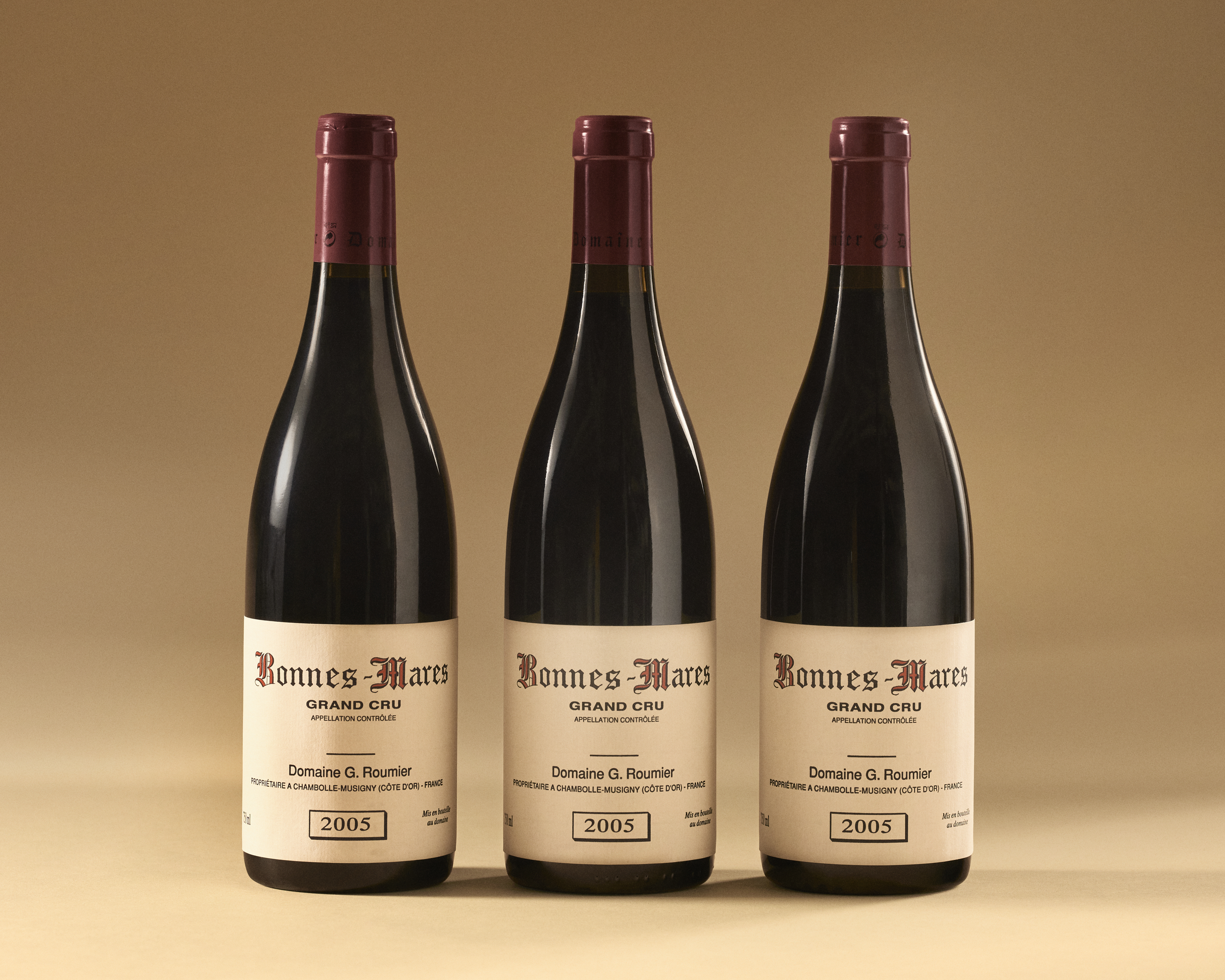 Three bottles of 2005 Domaine G. Roumier Bonnes-Mares Grand Cru red wine on a beige background.