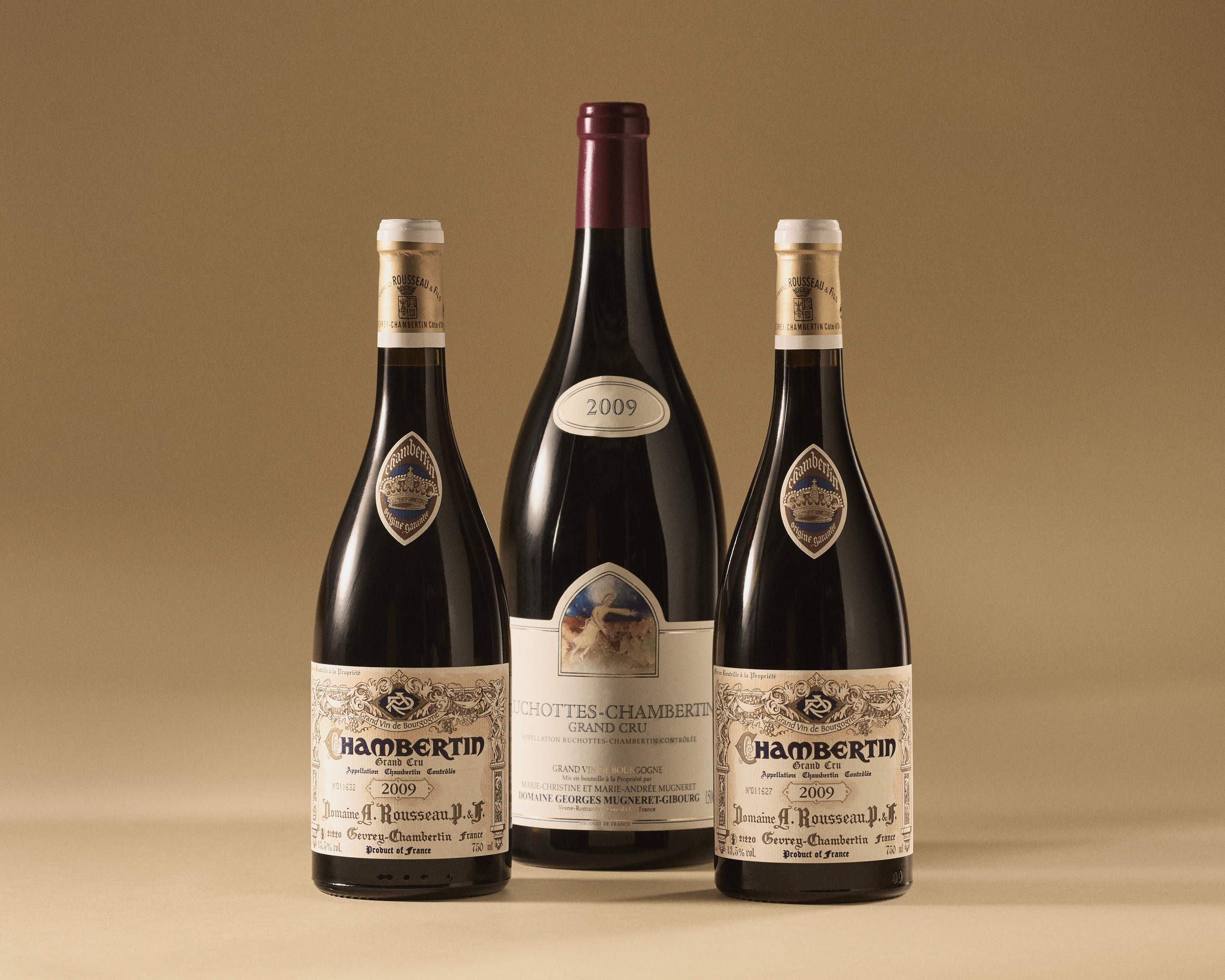 Three bottles of Chambertin Grand Cru wine from Domaine Armand Rousseau, vintage 2009, are displayed against a beige background.