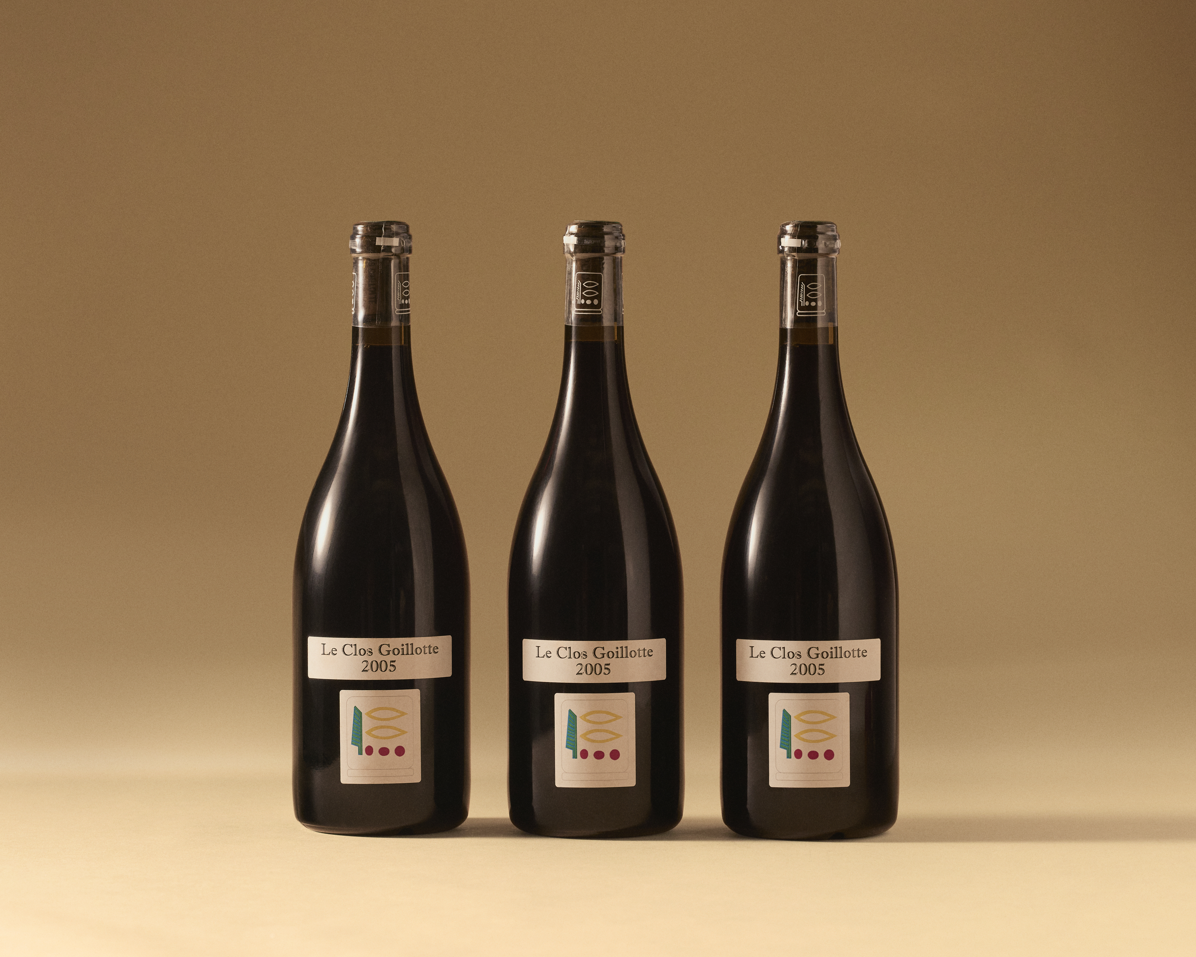 Three dark glass wine bottles labeled "Le Clos Guillotte 2005" are arrayed against a soft beige background.