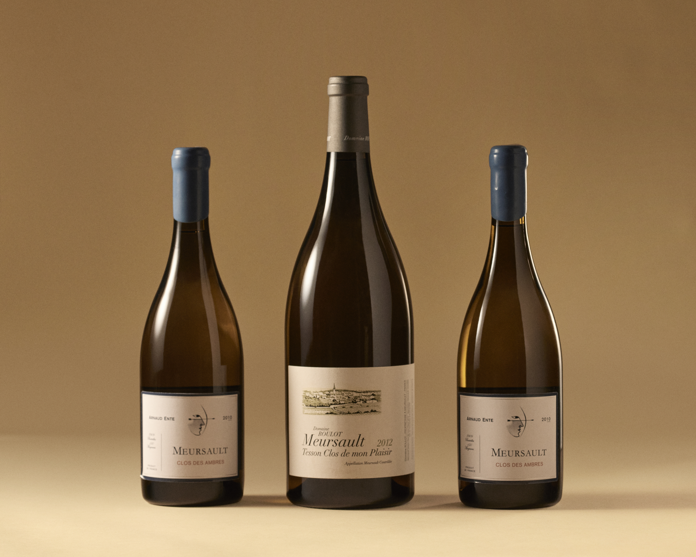 Three bottles of Meursault wine, each with a different label, stand against a beige background.