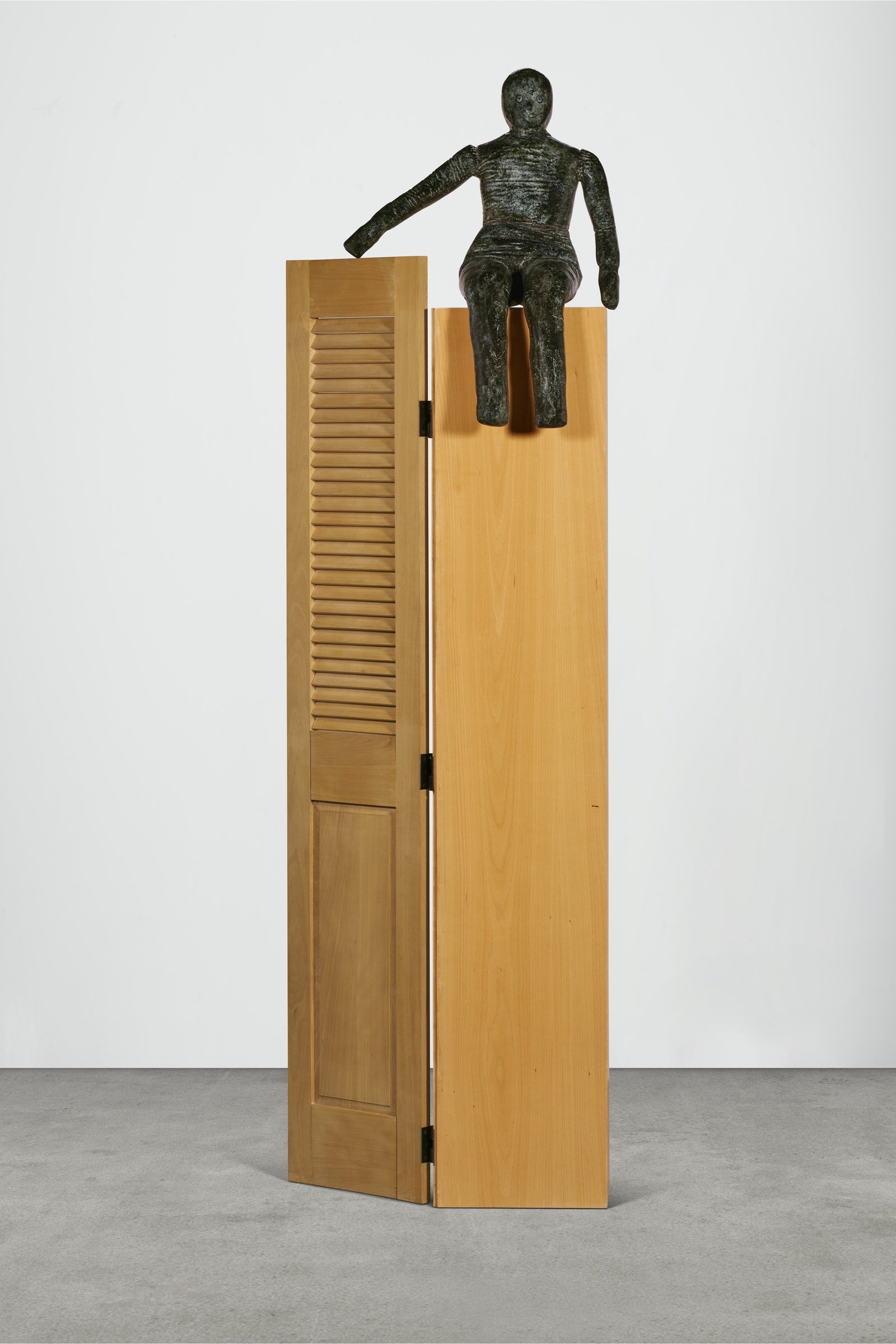 A sculpture featuring a bronze figure seated atop a tall, wooden cabinet with one door slightly ajar.