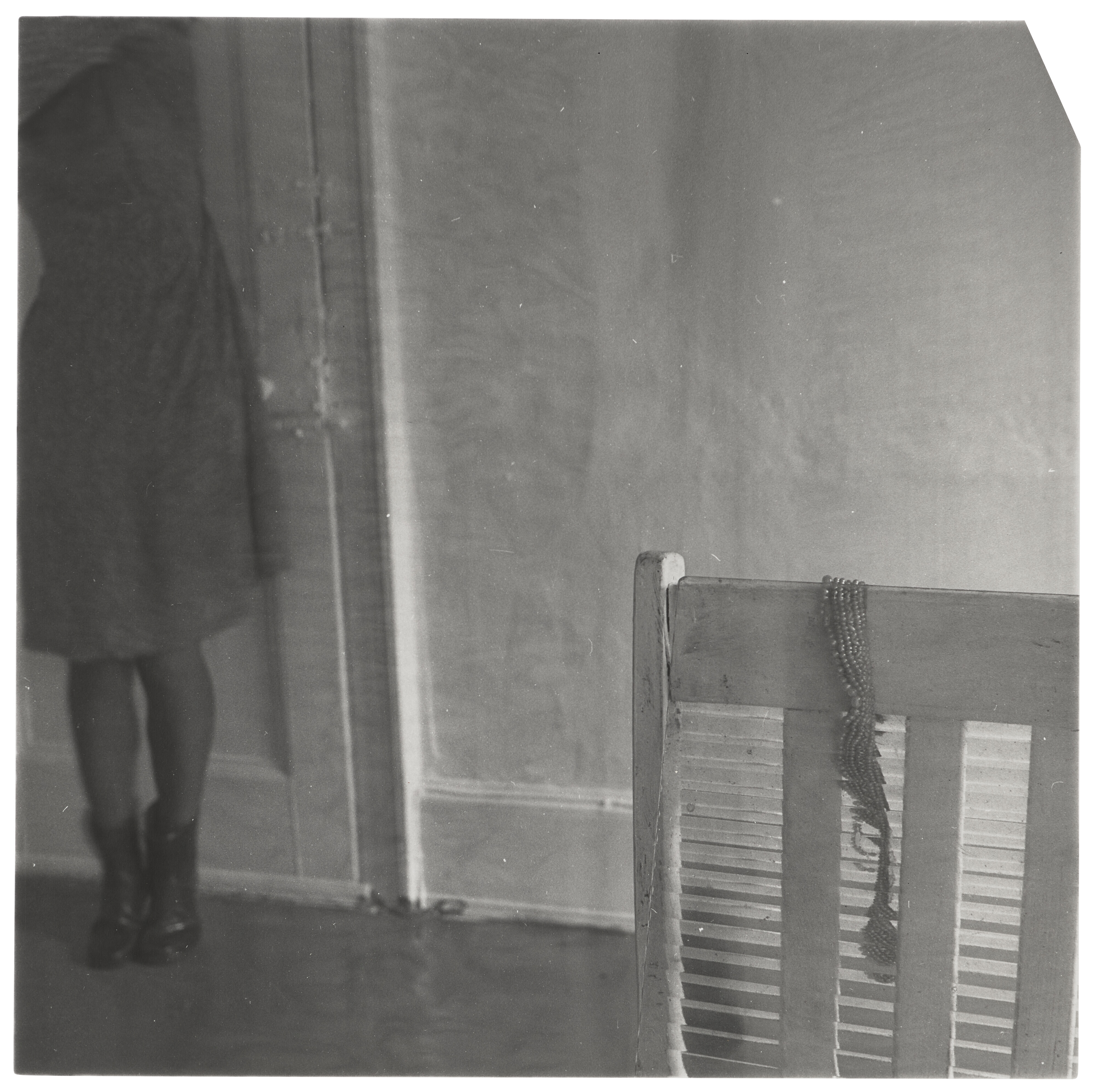 A black-and-white photo featuring a partially visible person next to a door and a wooden crib with beads hanging on it.