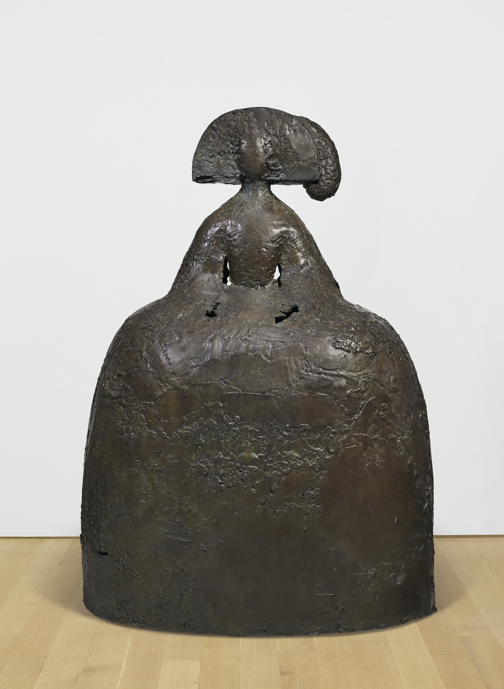 A bronze sculpture of a stylized female figure with a large, flowing headdress and textured, formless body.