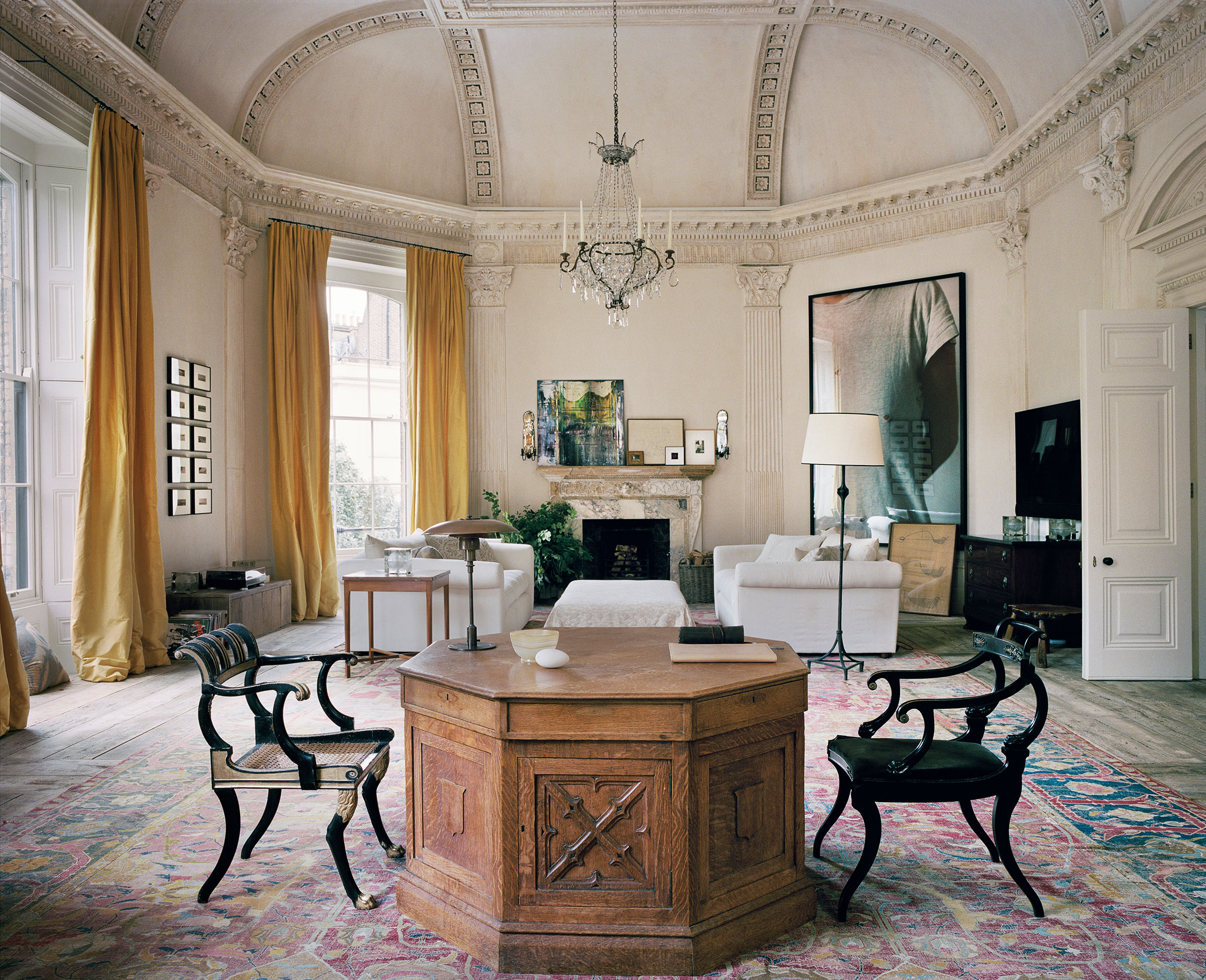 The study, formerly the ballroom, in Uniacke's Pimlico home. 'The volume is immense and absorbs colour, so sunshine yellow doesn't take over,' says the designer, who adds that there are 'two ebonised chairs on either side of the octagonal partner’s desk, all three from the Regency period'. On the floor is a 17th-century Mughal carpet; on the desk a Poul Henningsen lamp
