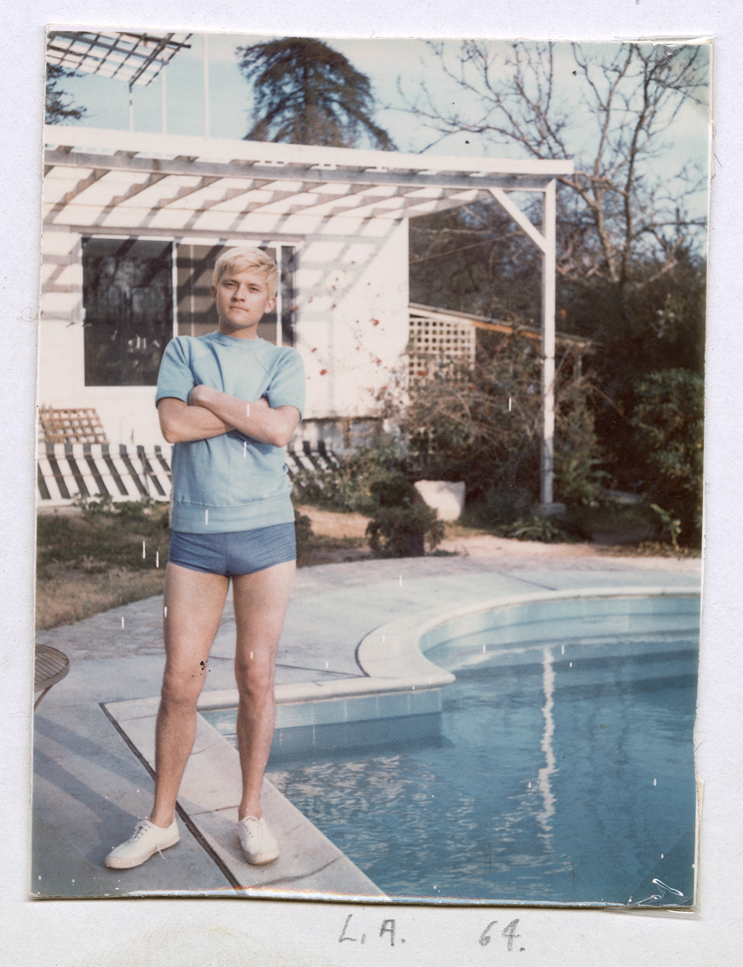 A vintage photo from 1964 showing a person standing by a pool in front of a house with a pergola, marked "L.A. 64." on the bottom.