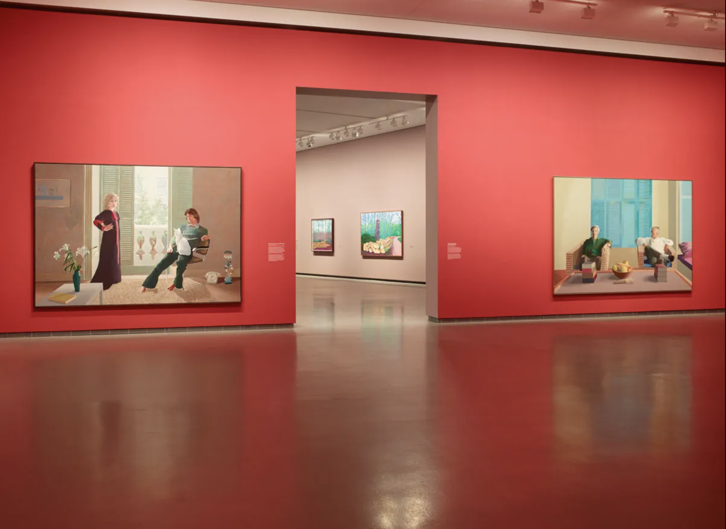A modern art gallery with large portrait paintings on bold red and neutral walls.