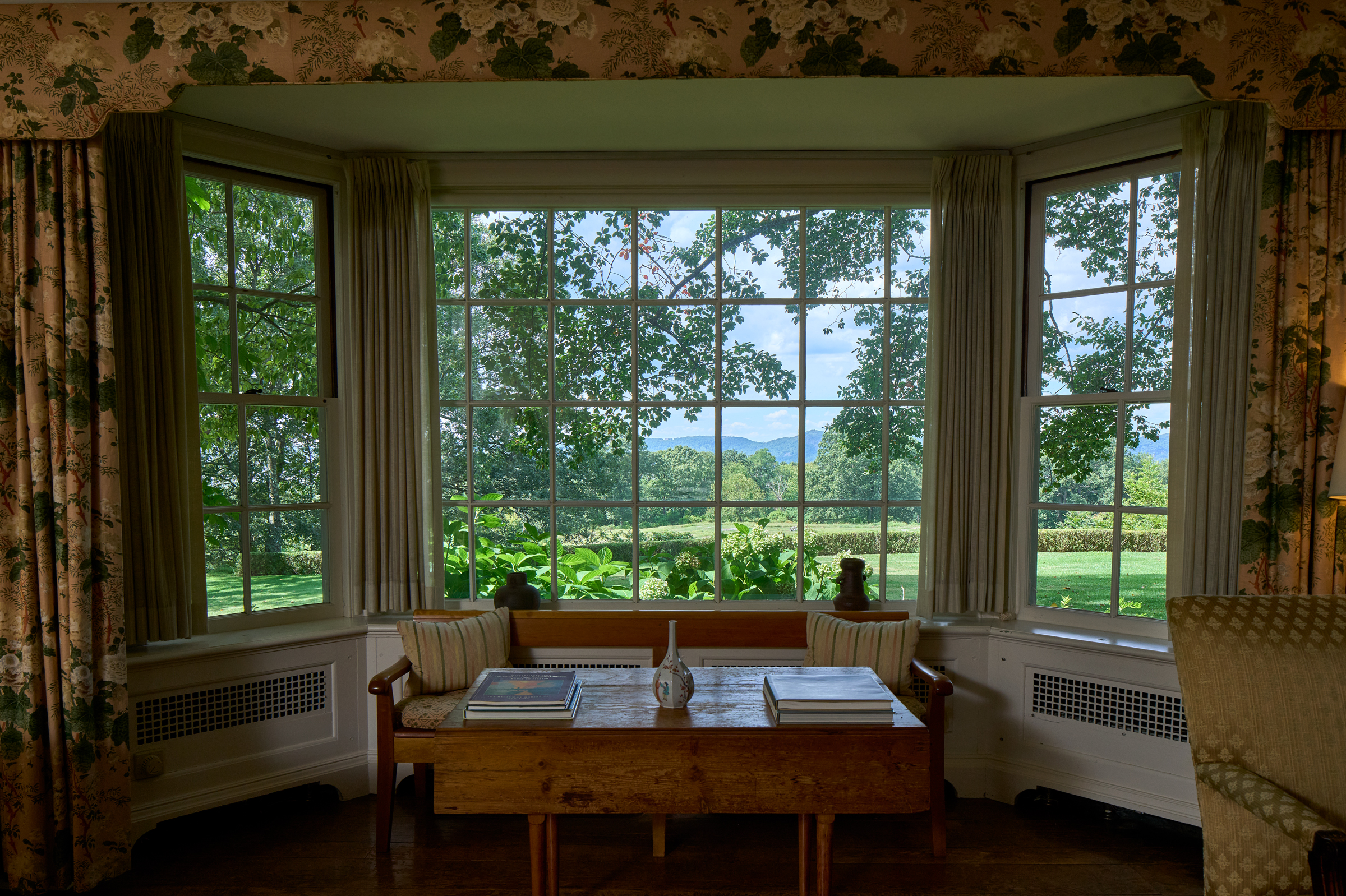 A cozy room with a large window showcasing a stunning view of green fields and distant hills.