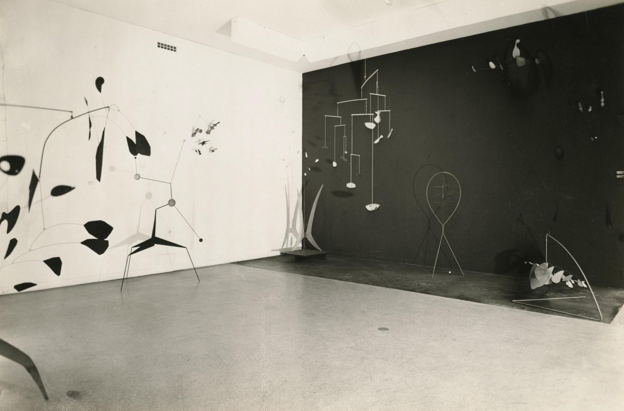 Art installation featuring abstract and geometric mobiles in a room with contrasting black and white walls.
