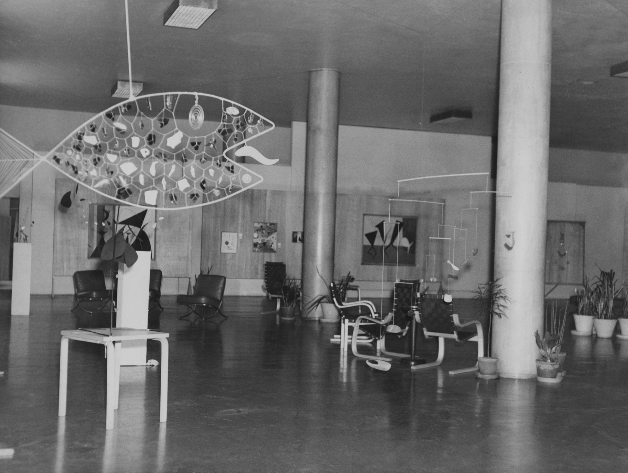 Black and white photo of a modern interior with sculptural fish art hanging from the ceiling and stylish furniture.