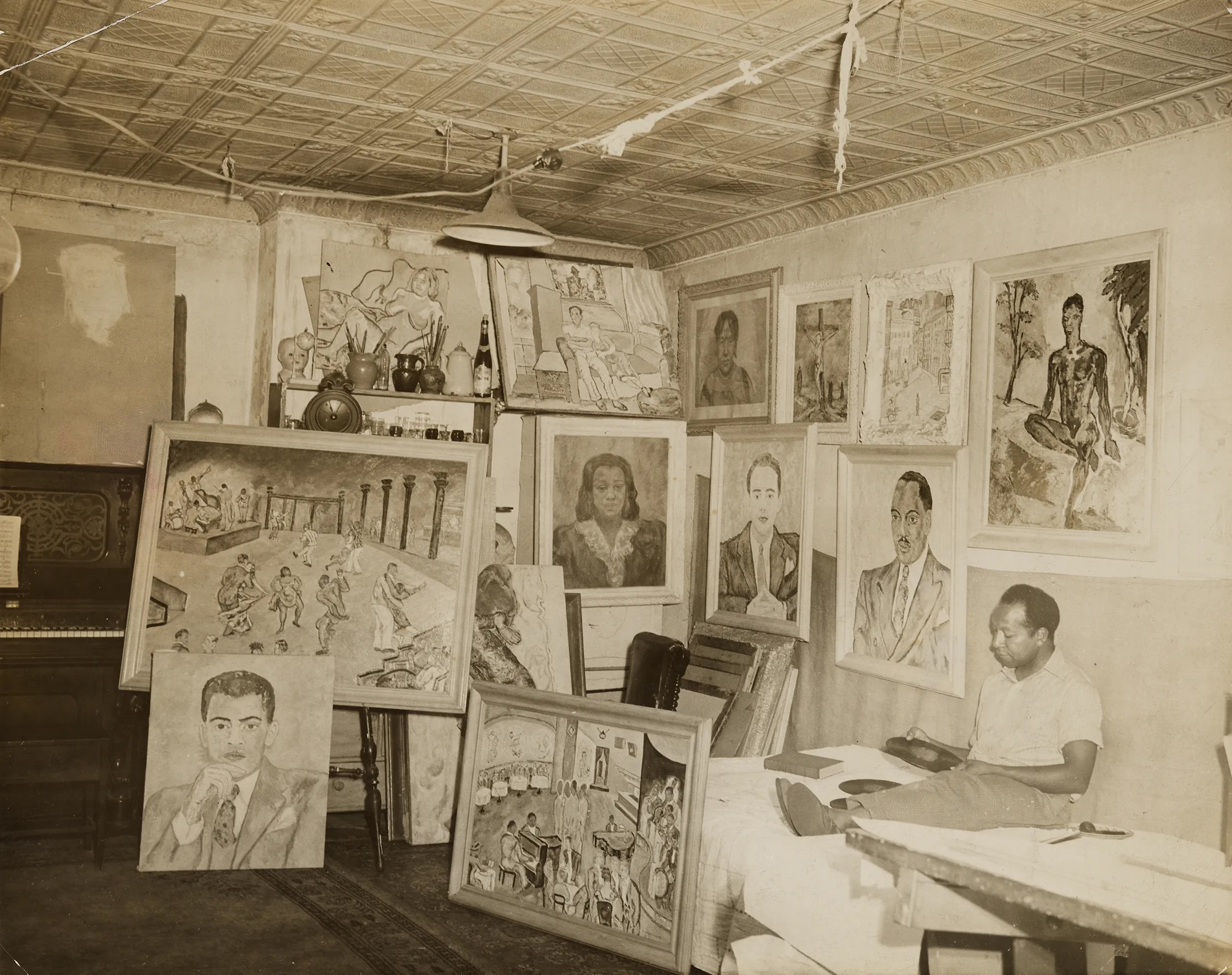 An artist's studio filled with various paintings, sketches, and an upright piano, showcasing diverse artwork on walls and easels.