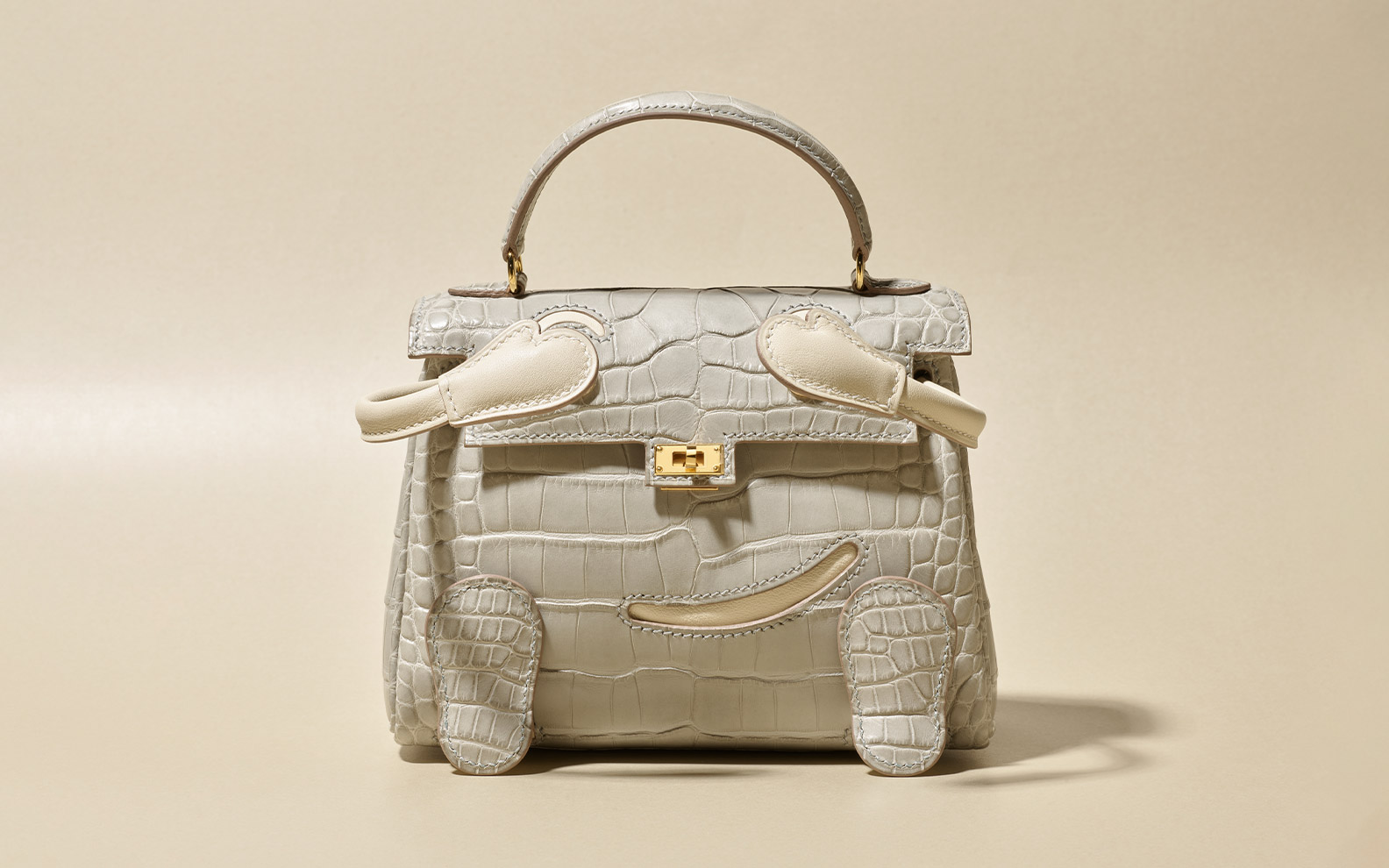 A light gray, crocodile-skin textured handbag with a unique elephant design, featuring gold hardware.