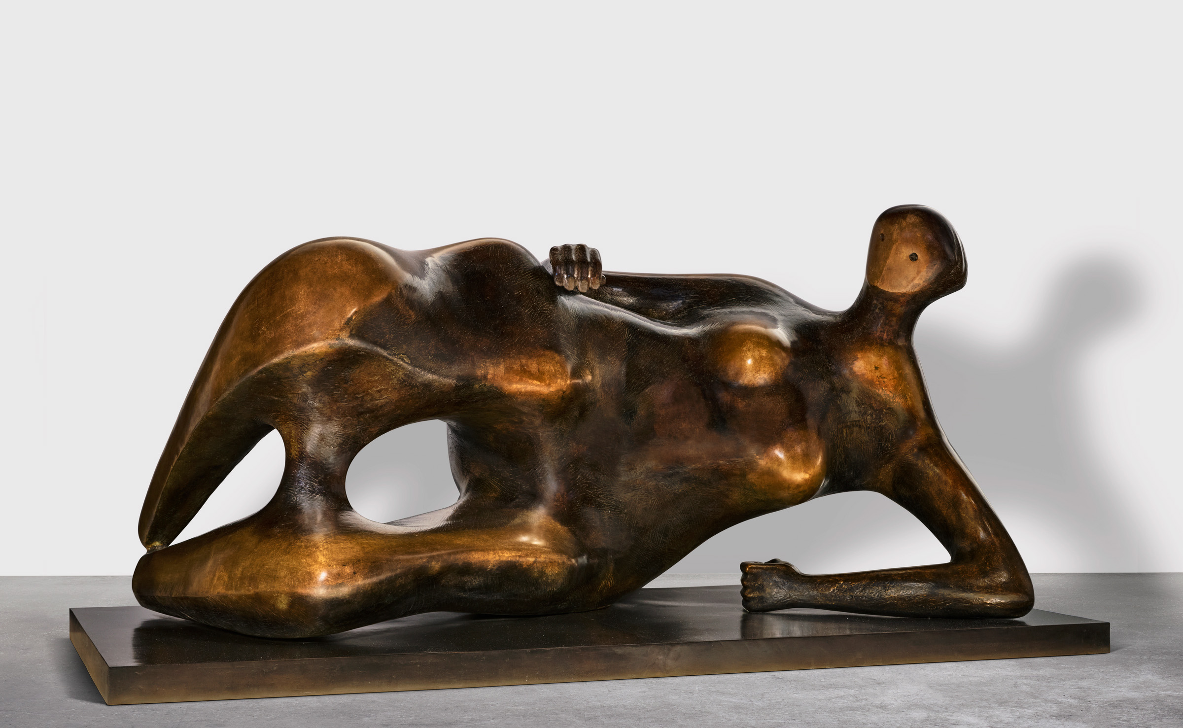 Bronze sculpture depicting a reclining figure with stylized, elongated forms and smooth, reflective surface.