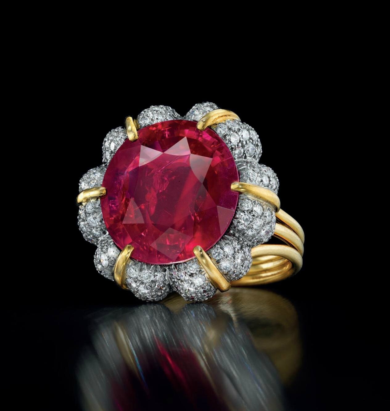 A luxurious ring featuring a large red gemstone, surrounded by sparkling diamonds set in gold prongs and band.