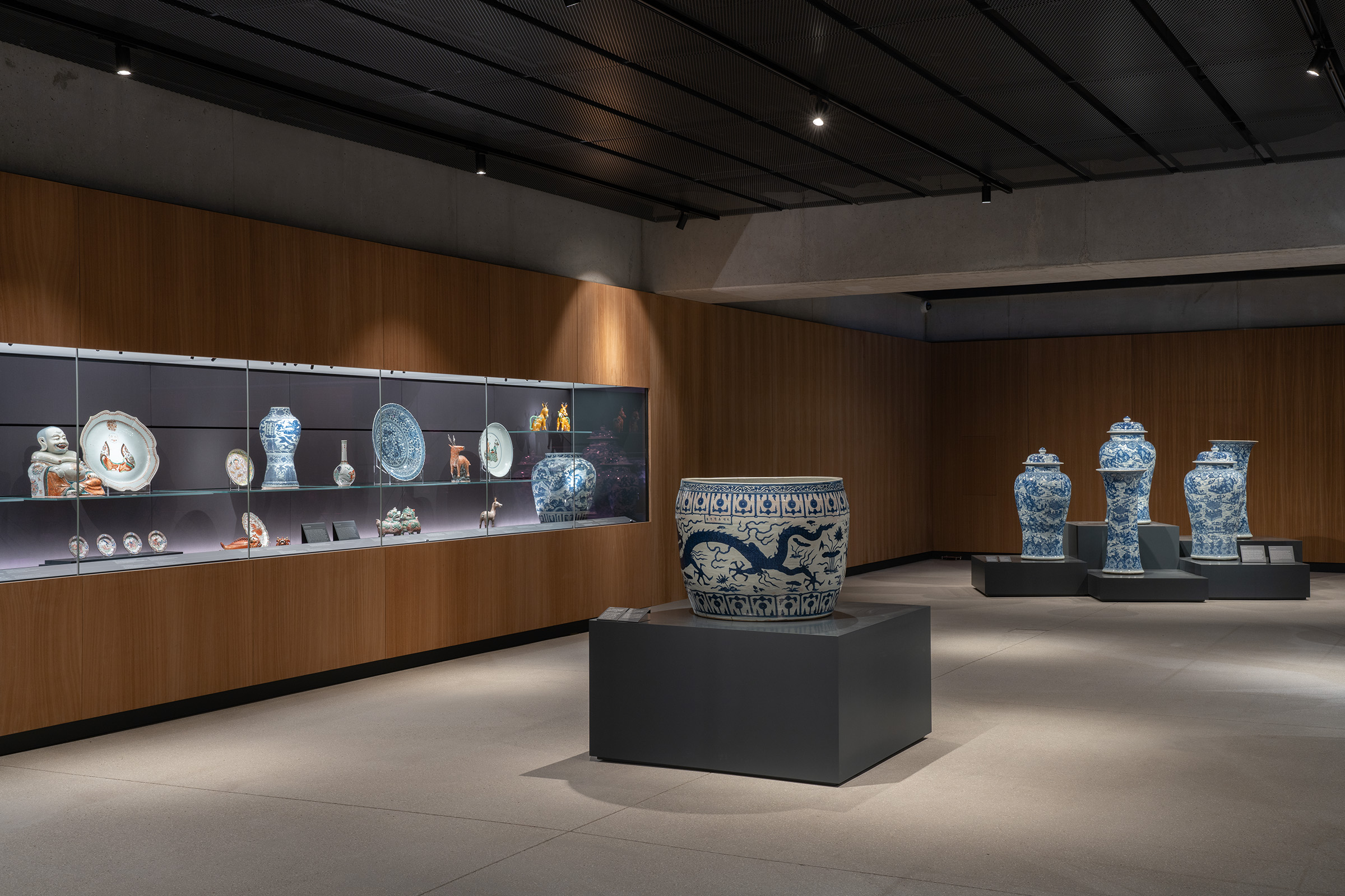 Installation view of Connections: Works from the Albuquerque Collection. On the right is a Qing dynasty porcelain five-piece garniture painted with scenes of West Lake in underglaze blue. China, Kangxi period (1662-1722), circa 1700. A Ming dynasty fish bowl decorated with five-clawed dragons, Jiajing period (1522-1566), stands in the centre of the room. In the cabinet to the left is a Qing dynasty porcelain tureen in the form of a laughing Buddha, Qianlong period (1736-95), circa 1770-80
