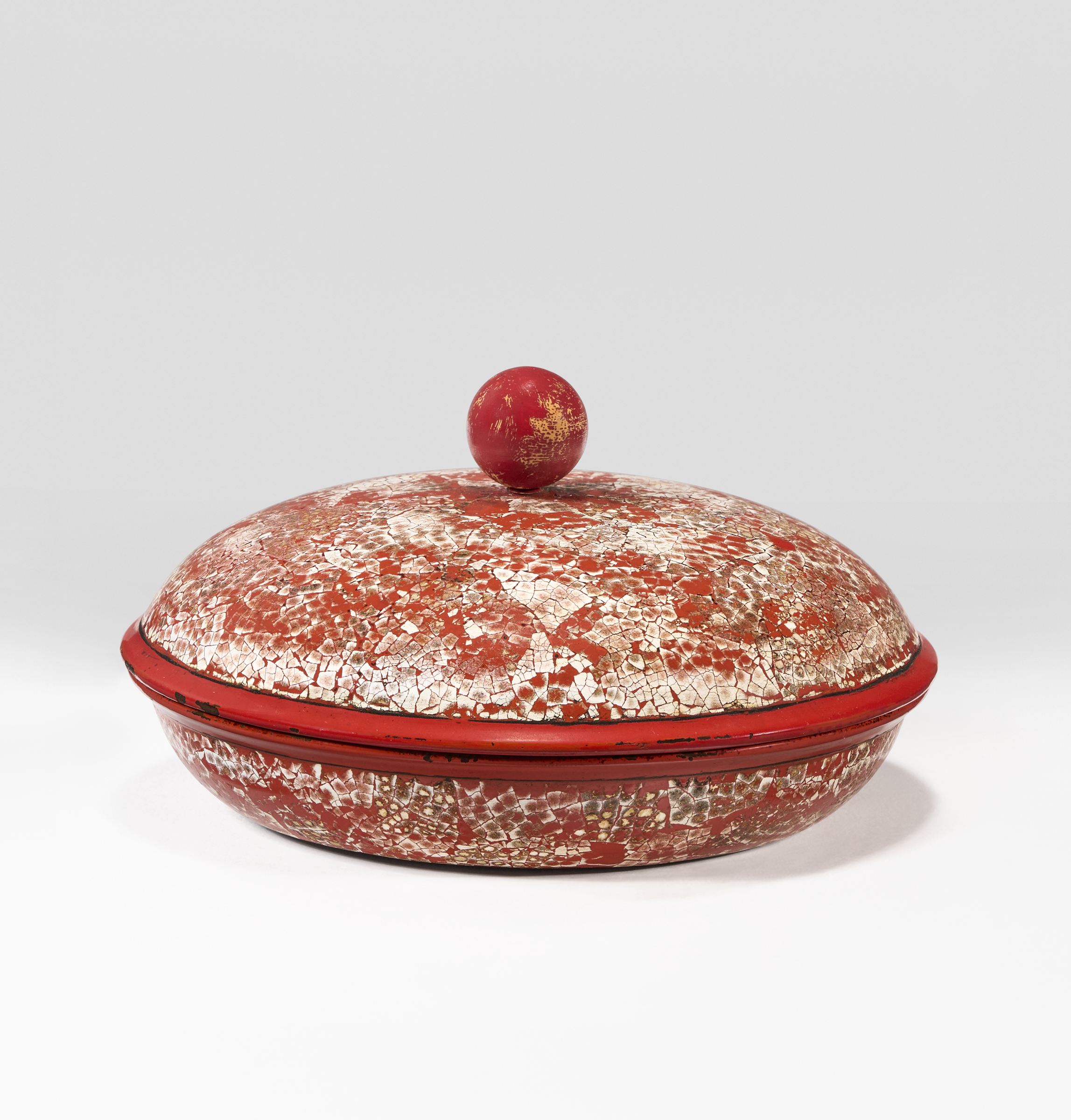 A round, lidded container with a red and white cracked finish, topped with a spherical knob, sits against a plain light background.