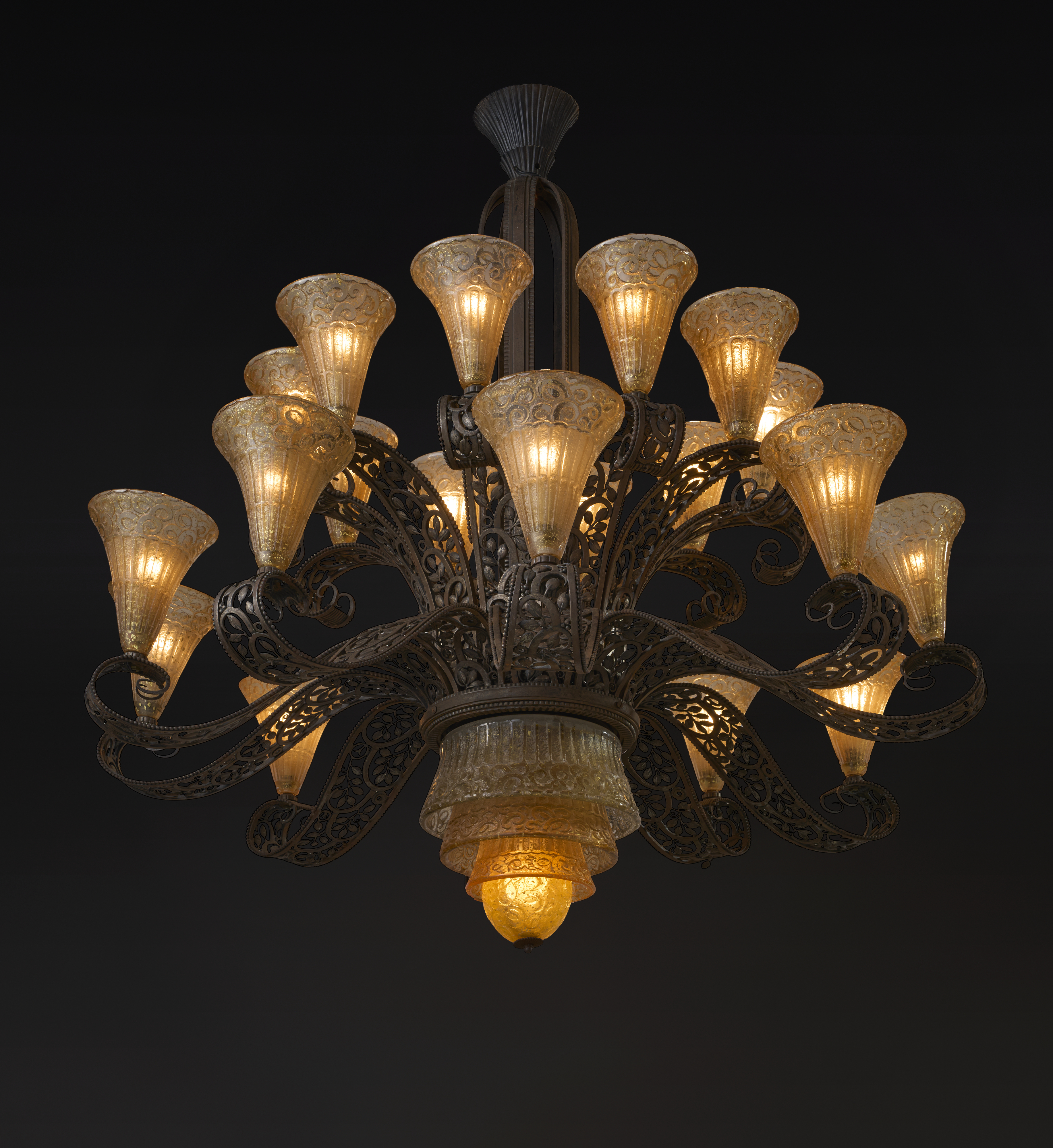An ornate chandelier with golden glass lamps and intricate metal scrollwork is illuminated against a dark background.