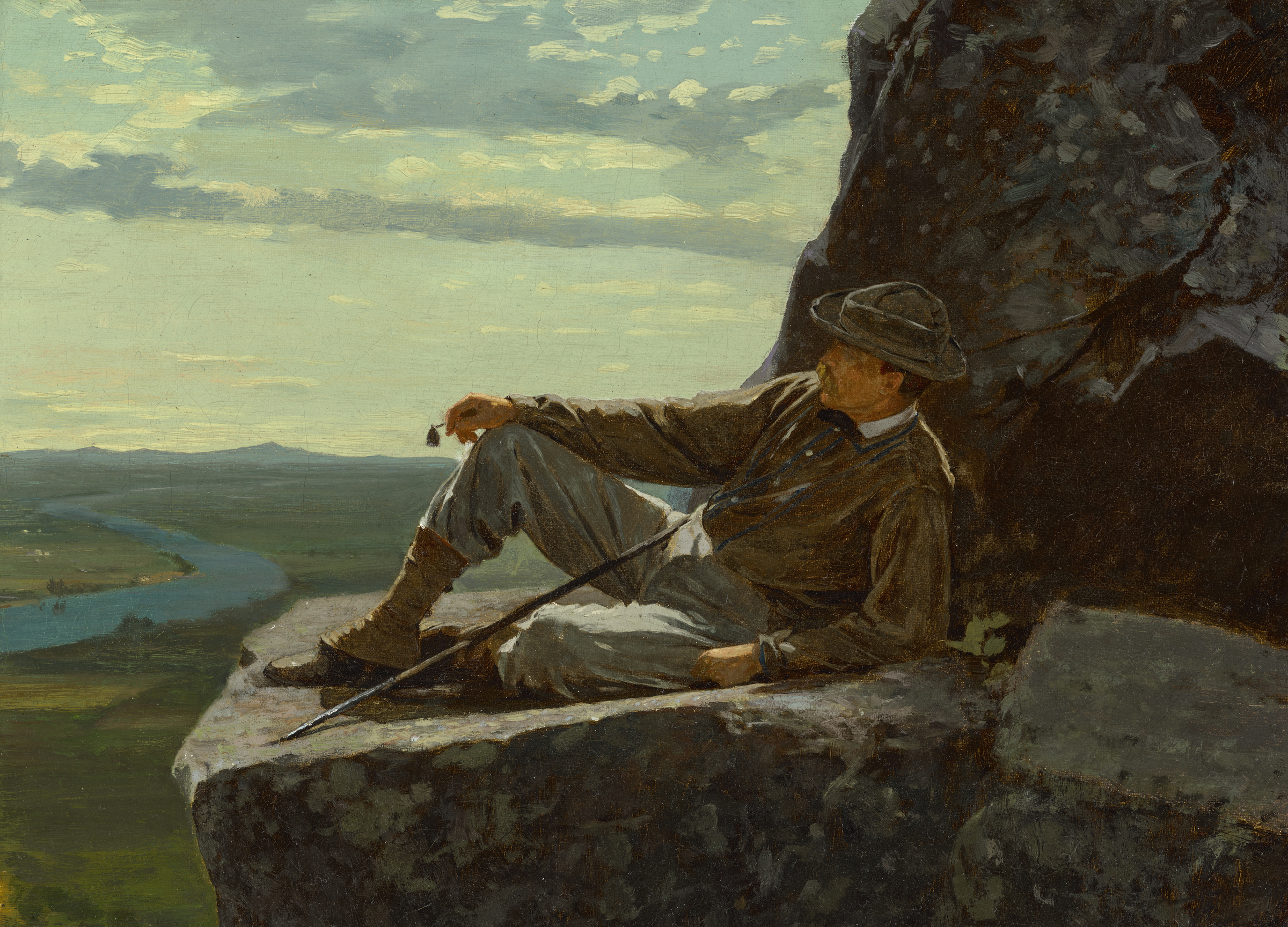 A man in outdoor clothing rests on a rocky ledge, gazing over a river and vast landscape below.